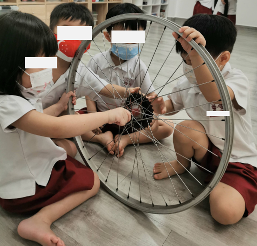 Group of toddlers examining and exploring a bicycle wheel rim together.