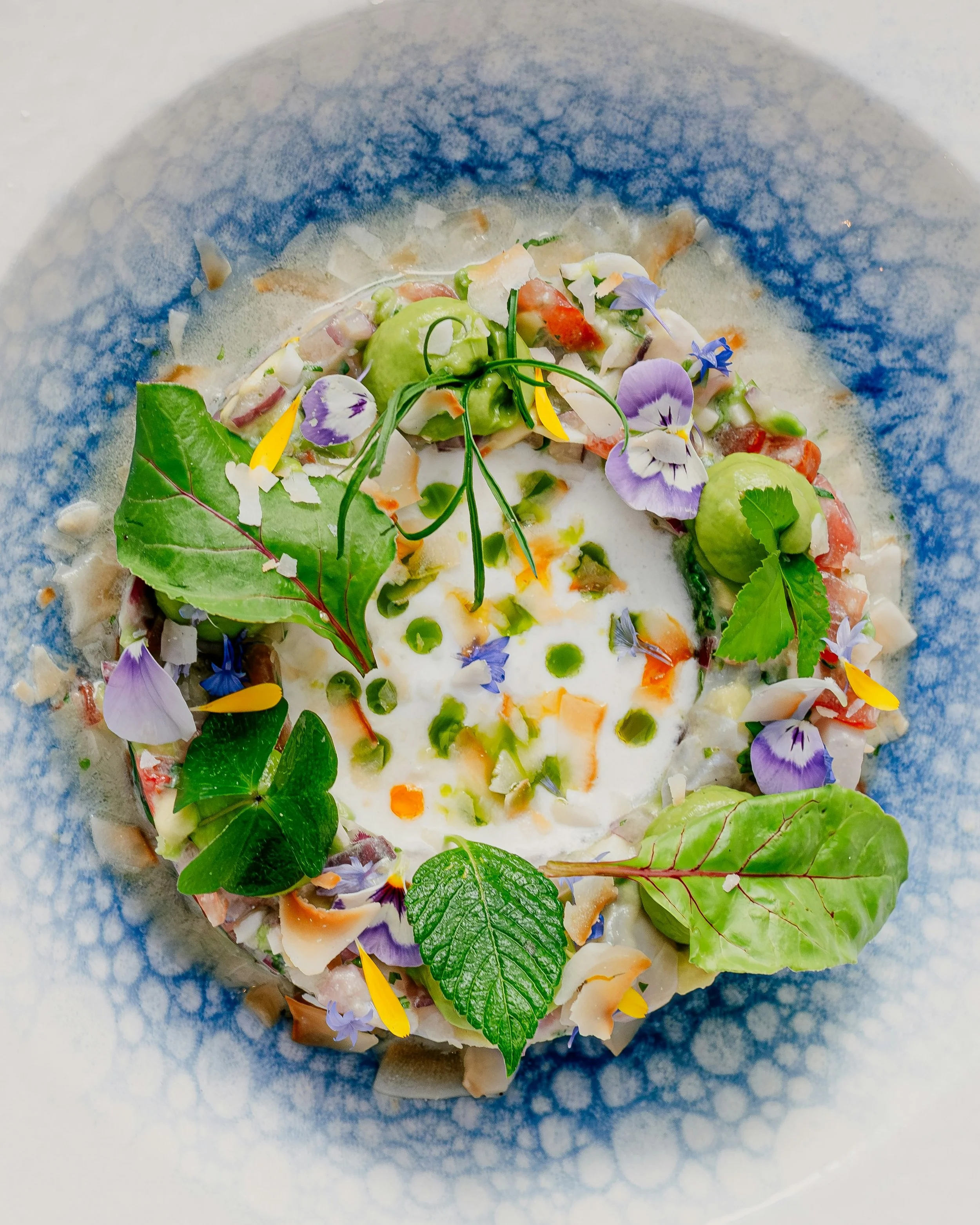 Elegant plate with a fine dining dish, decorated with edible flowers, green vegetables, and colorful garnishes.