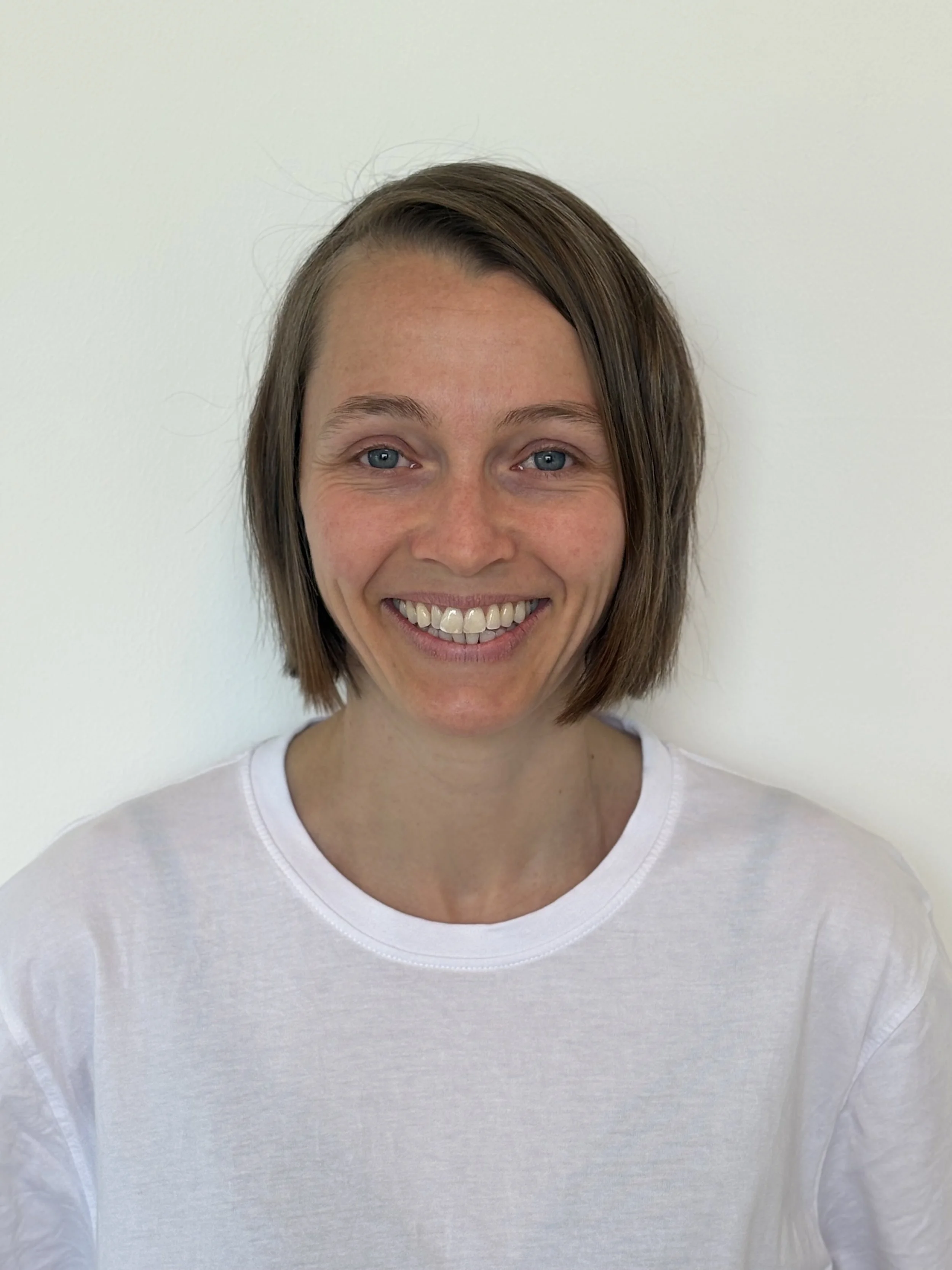 Ein Lächelndes Mädchen mit braunen, kinnlangen Haaren vor einem weißen Hintergrund.