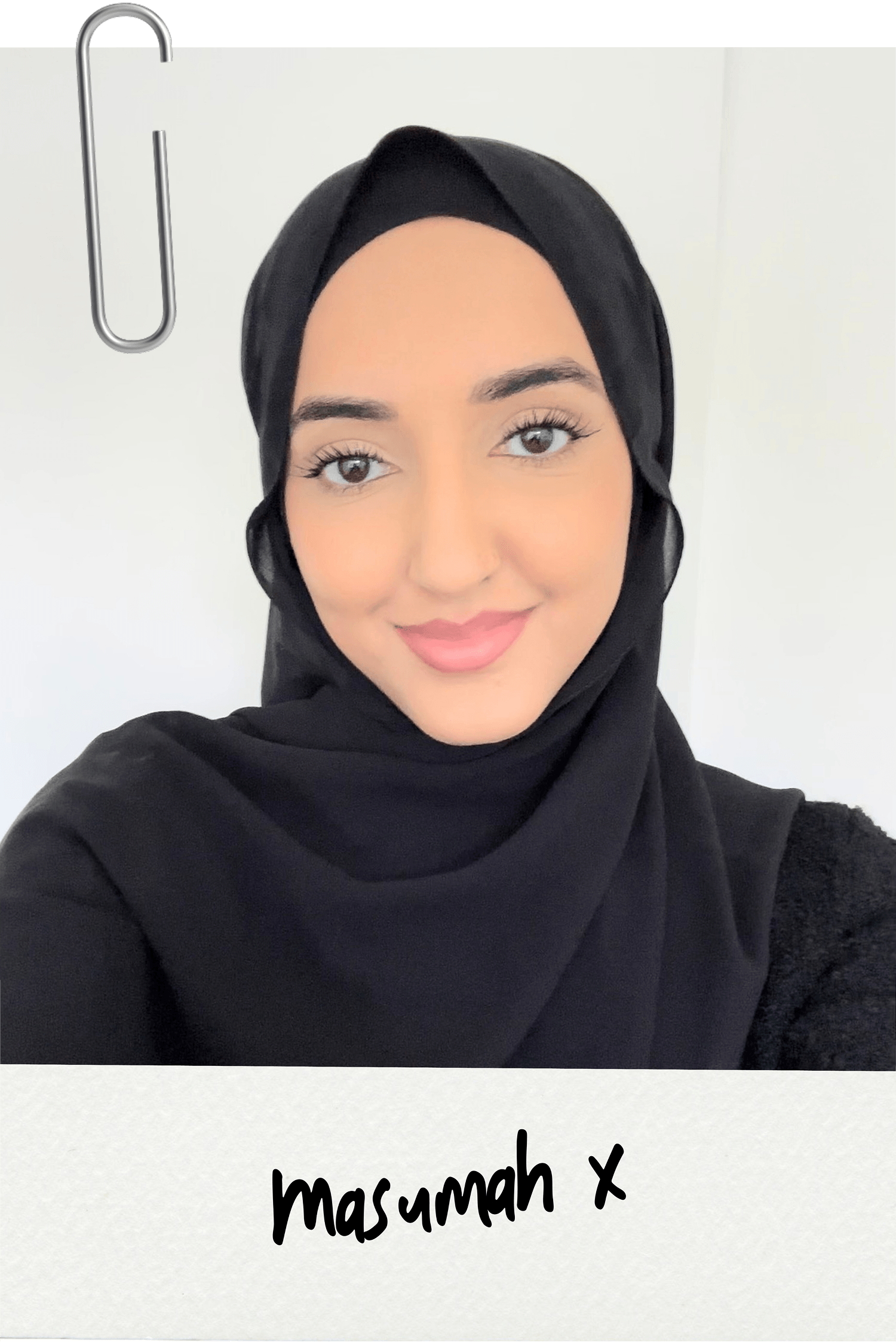 A woman wearing a black hijab smiling in a selfie, with a white background and a silver paperclip in the top left corner. She has light skin, brown eyes, and pink lipstick. The caption at the bottom reads 'masumah x'.