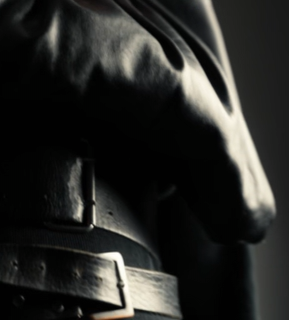 Close-up of a person's waist wearing a dark leather belt and jacket, highlighted by dramatic lighting.