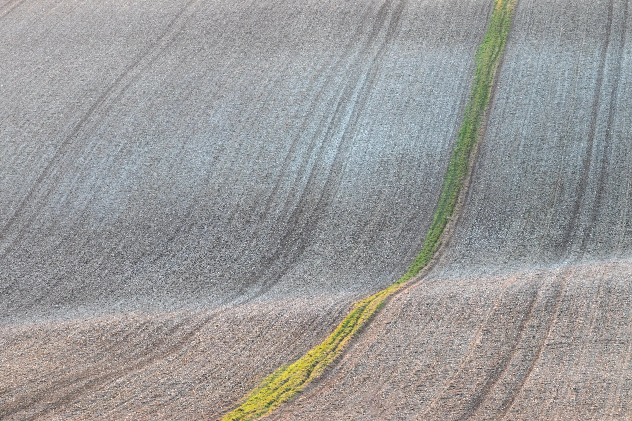 An aerial view of a vast, rippled ploughed field with a narrow green strip of grass running through the middle.