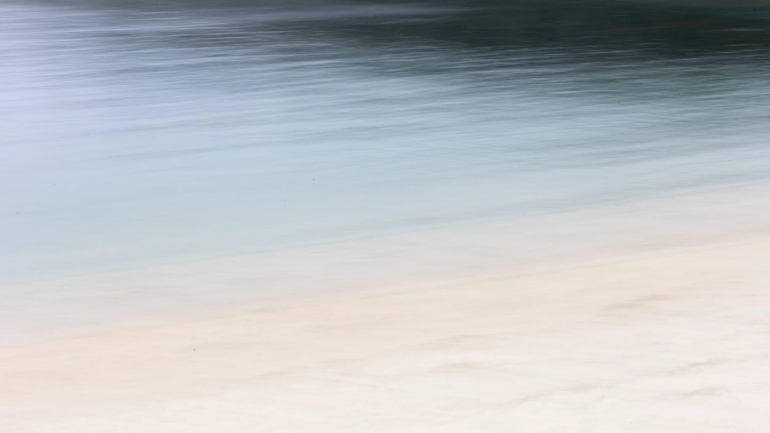 ICM photography creates a smoothly blurred image of a beach capturing the tones of sand in the foreground and ocean waves in the background.