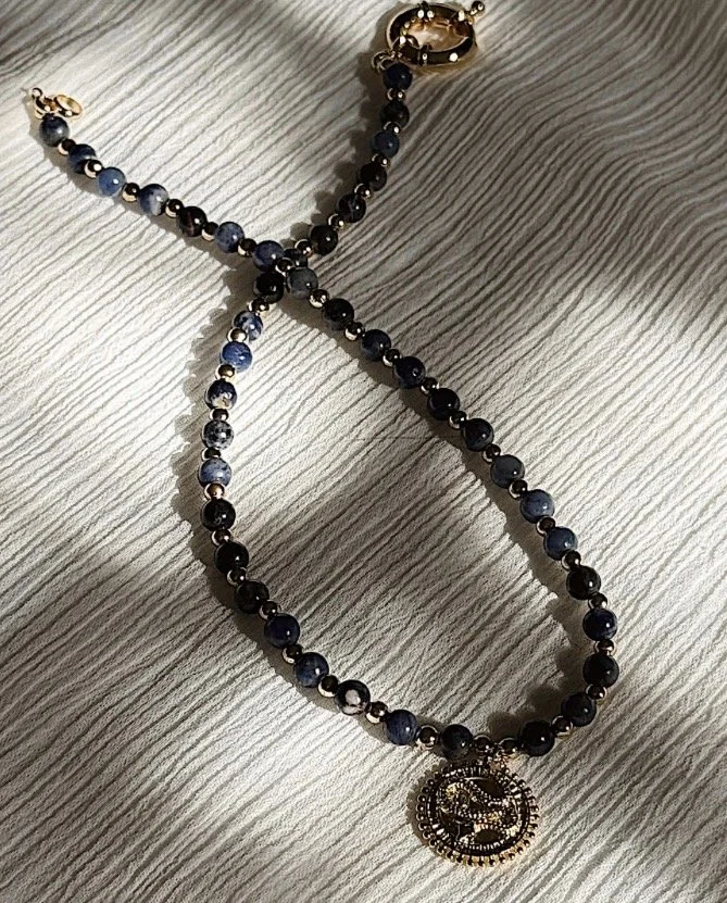 A beaded necklace with black and blue beads and a circular gold pendant lying on a wooden surface.