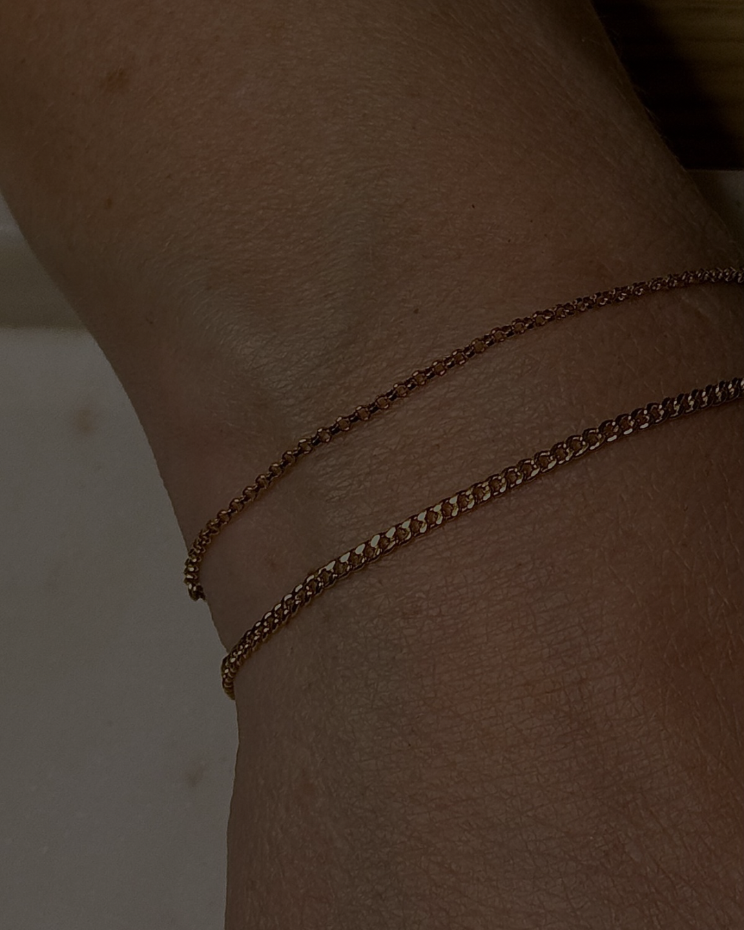 Close-up of a person's wrist with three thin gold chains worn around it.