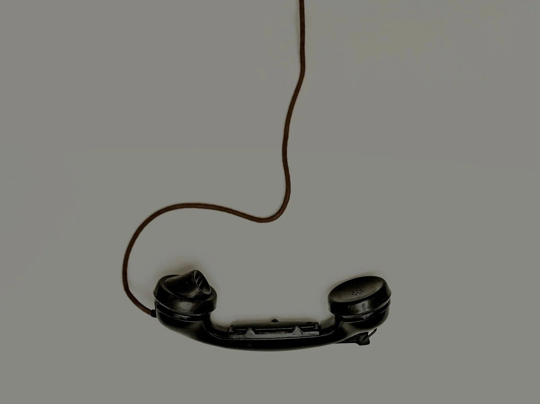 An old black rotary phone receiver with a brown cord against a light gray background.