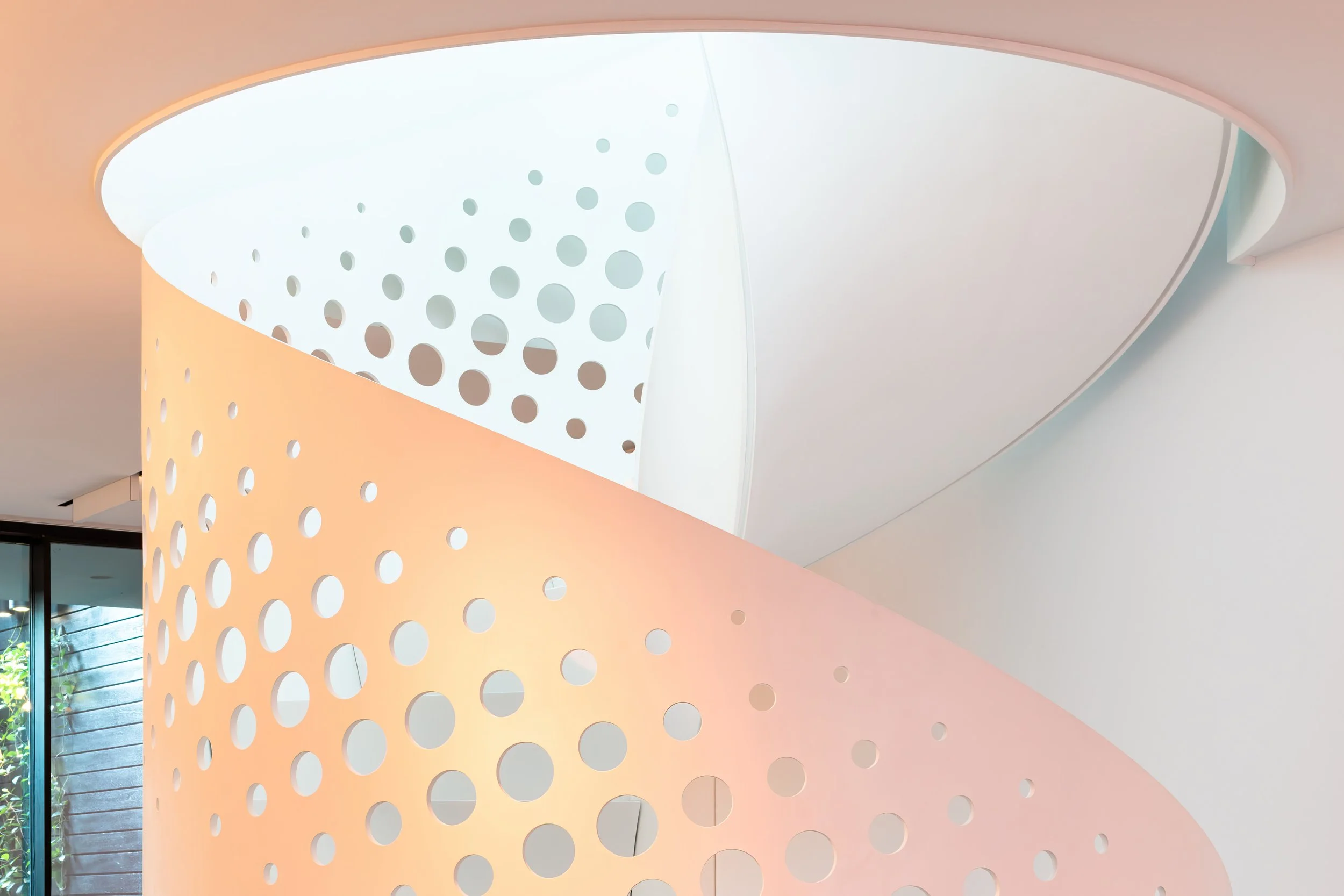 Modern interior with curved structures featuring circular cutouts, soft pastel lighting, and a large window showing greenery outside.