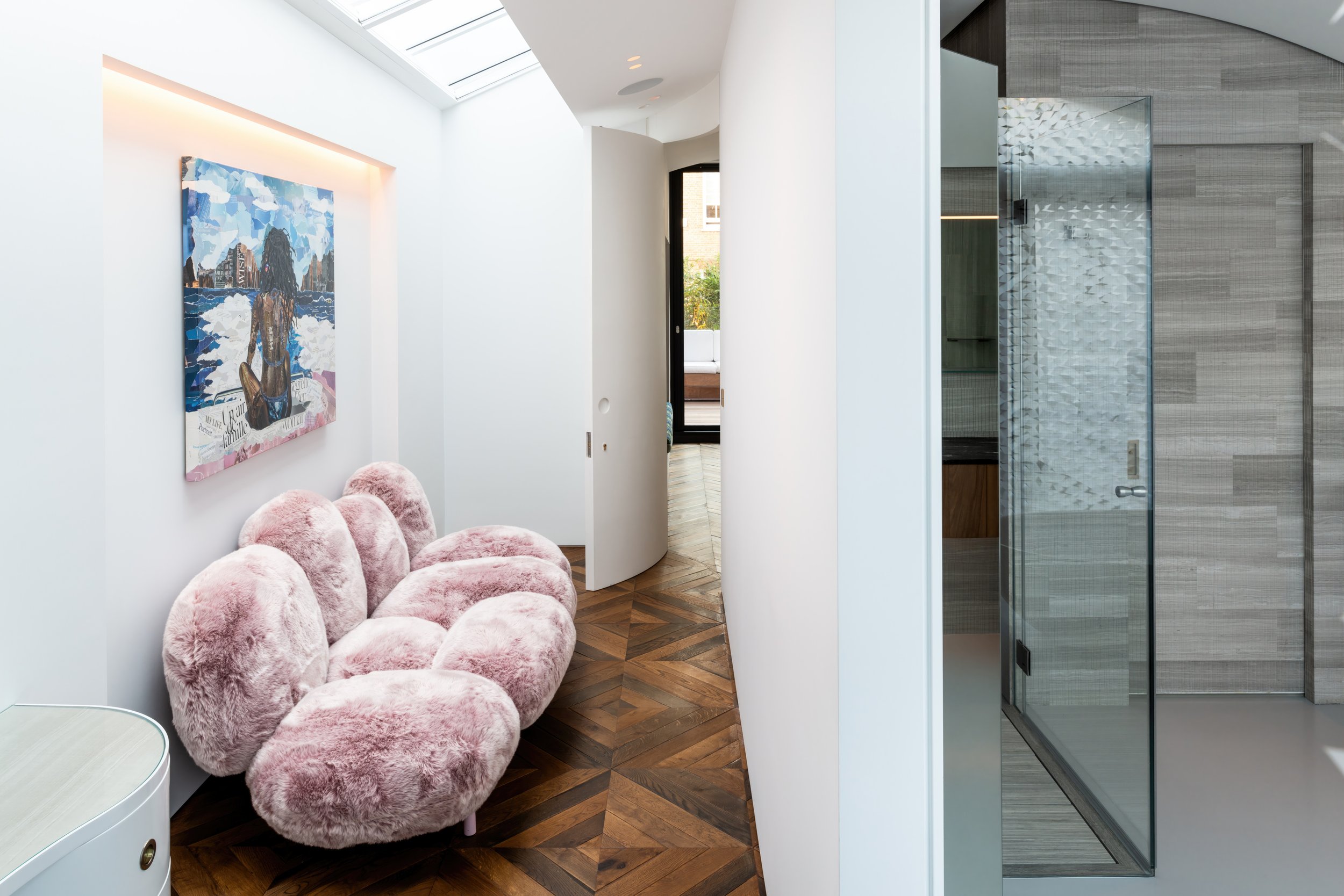Modern interior space with a pink furry sofa, a colorful artwork on the white wall, and a glass-enclosed shower area with wooden and tile accents.