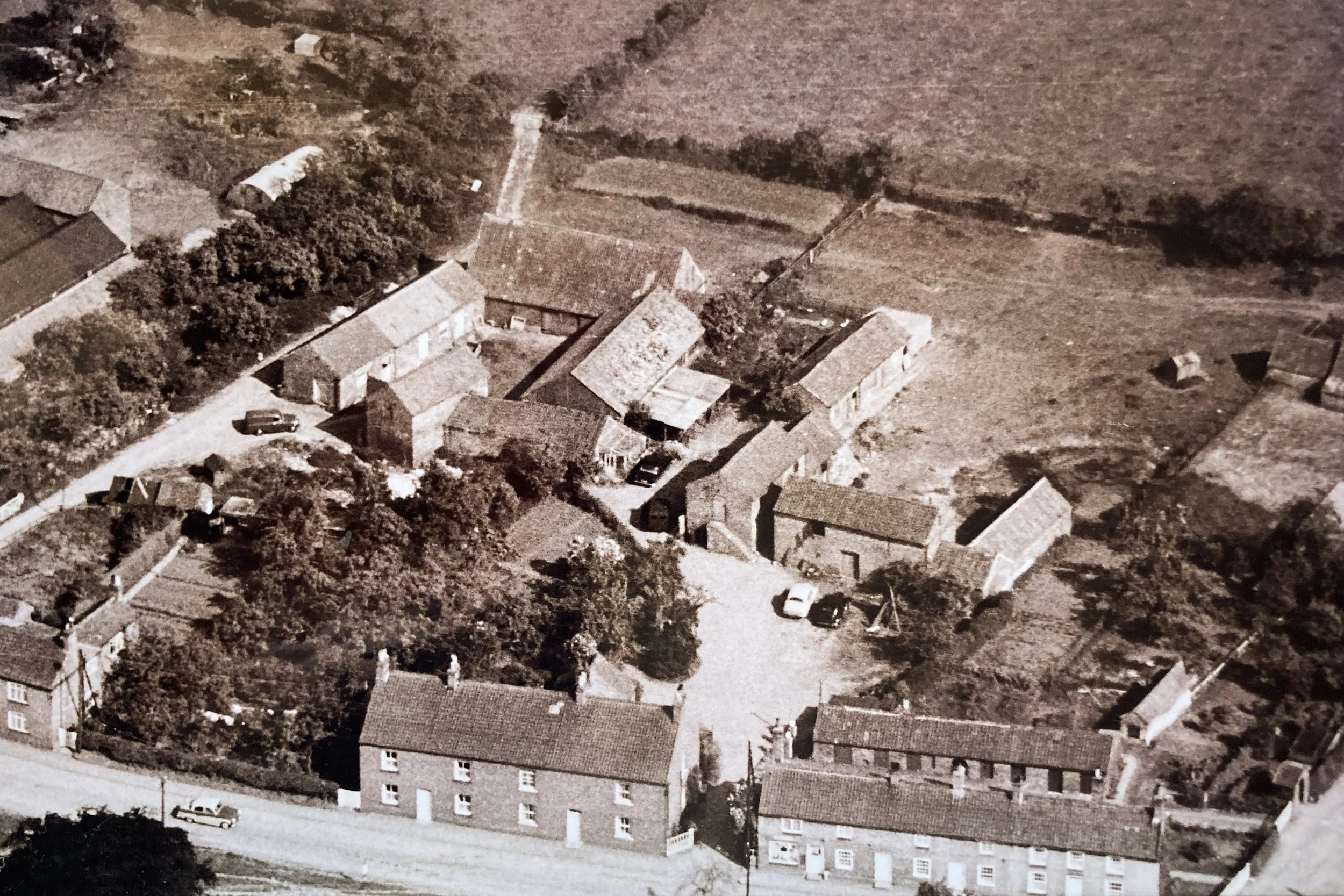 Aerial view of a small rural village with houses, trees, and unpaved roads.