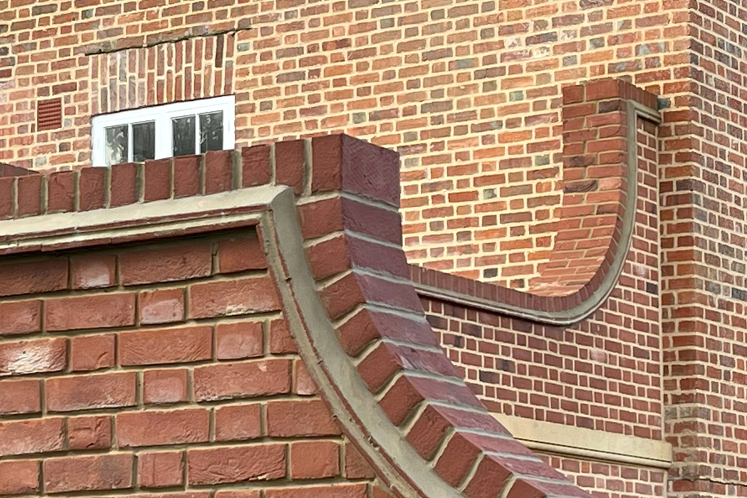 Close-up of a brick building corner with a curved brick detail and a small window, showing various shades of red bricks and mortar.