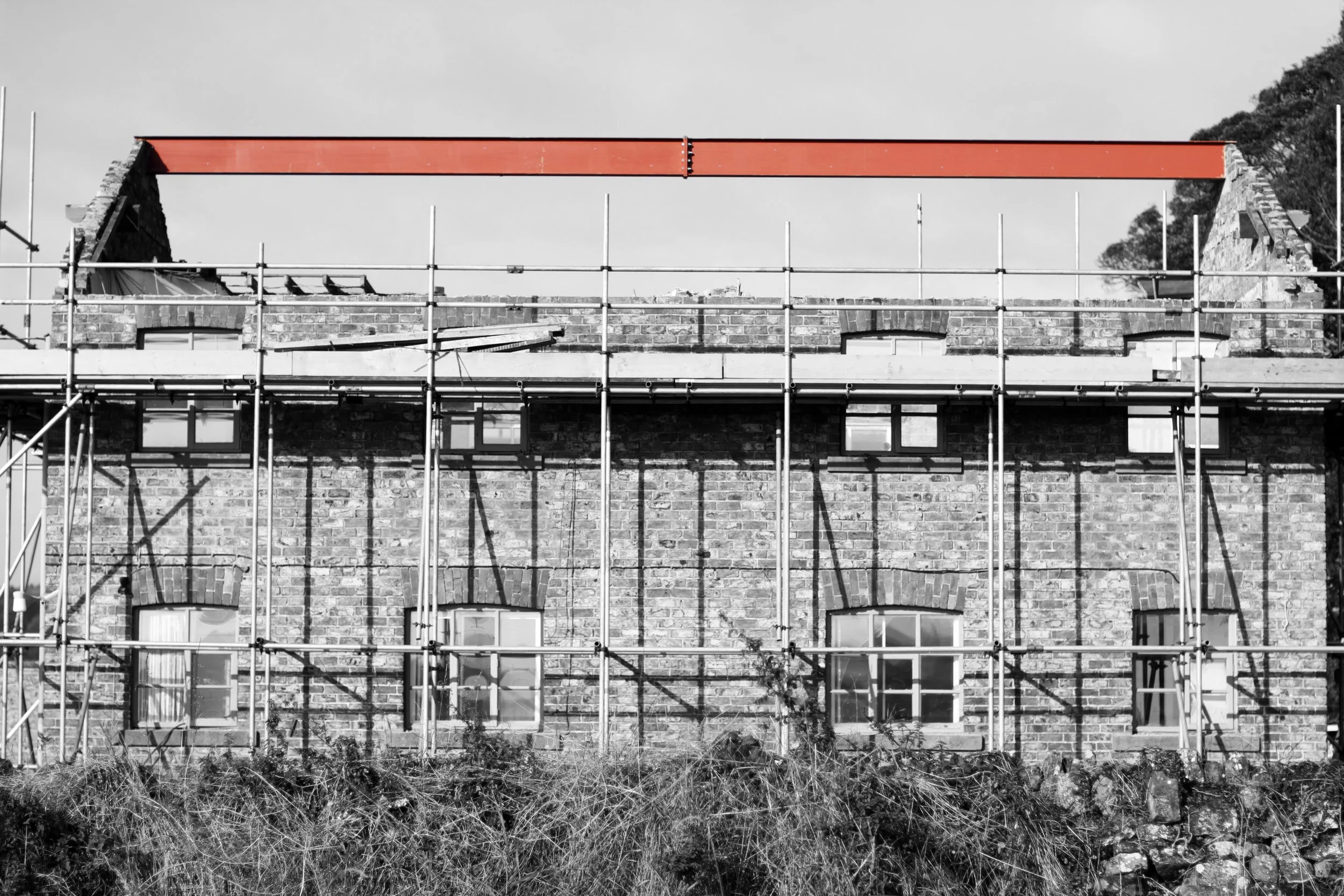A building under renovation with scaffolding and a red beam on top, black and white with selective color on the beam.