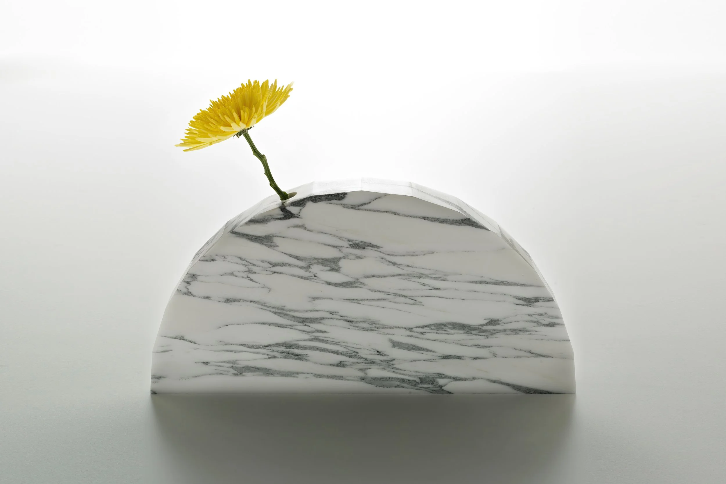Yellow flower in a white marble-shaped vase with gray veining, on a plain white background.