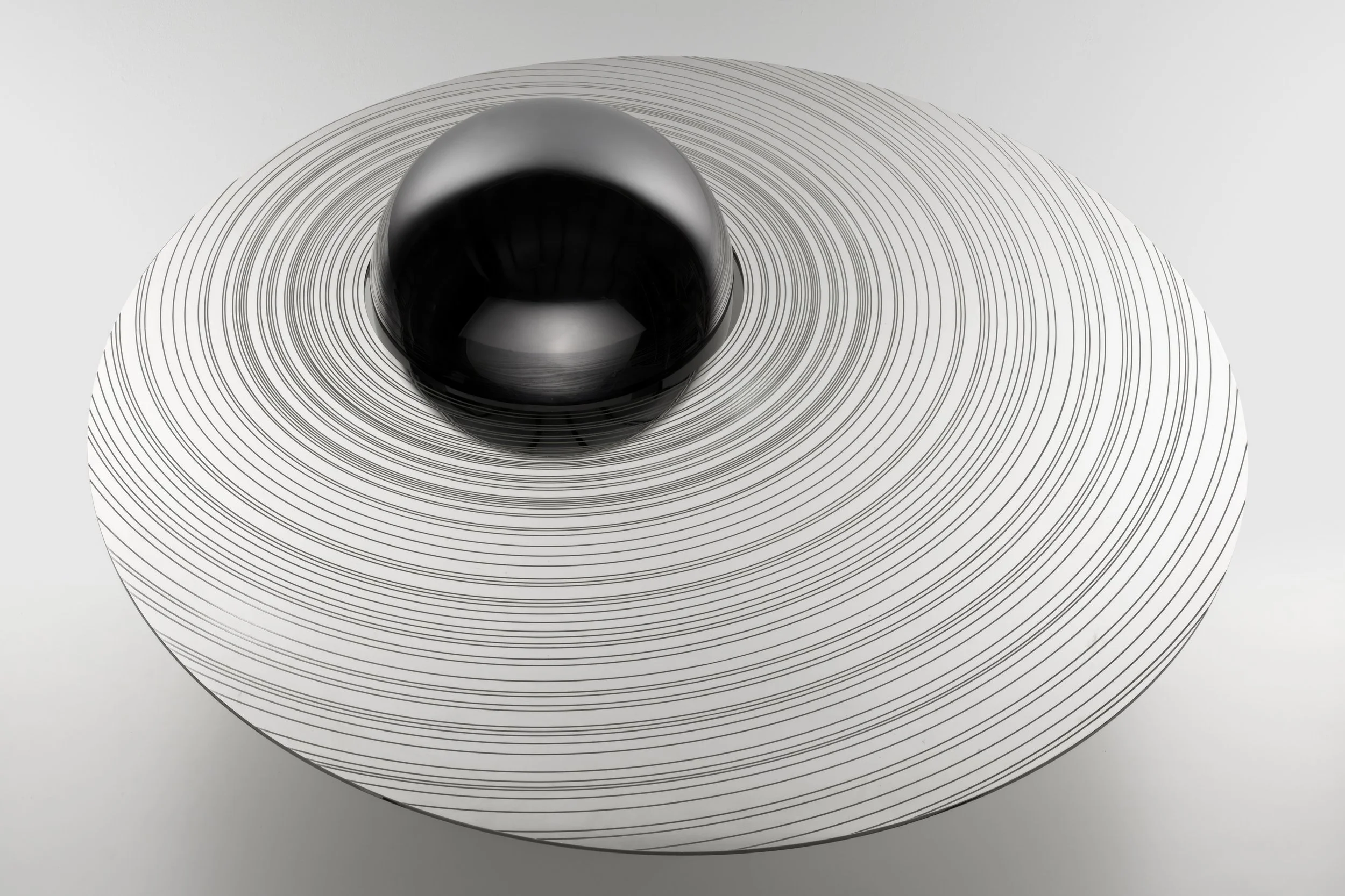 A black reflective sphere resting on a white circular surface with concentric black lines.