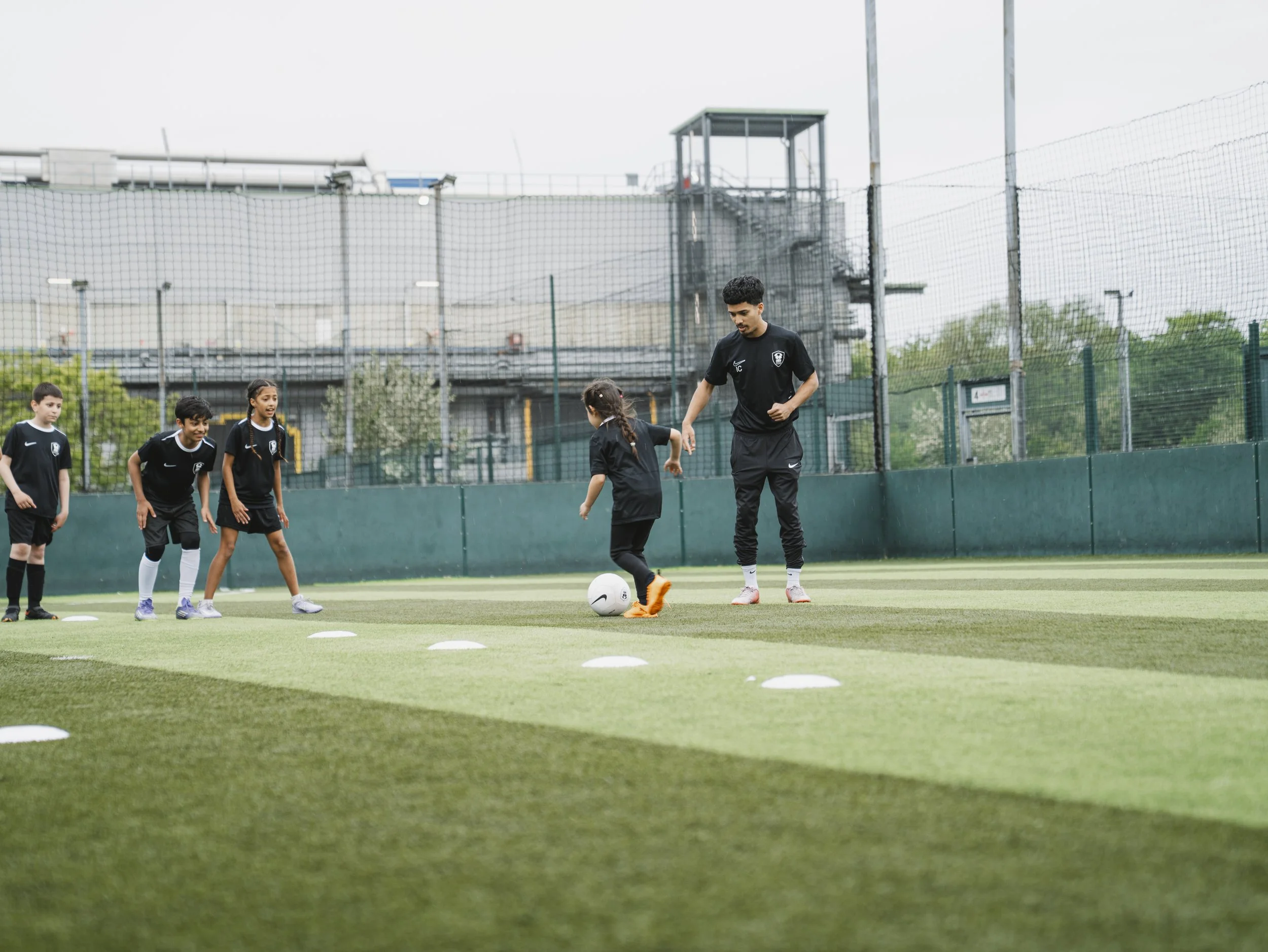 Young boys and a coach on a soccer field, practicing dribbling with a soccer ball during a training session.