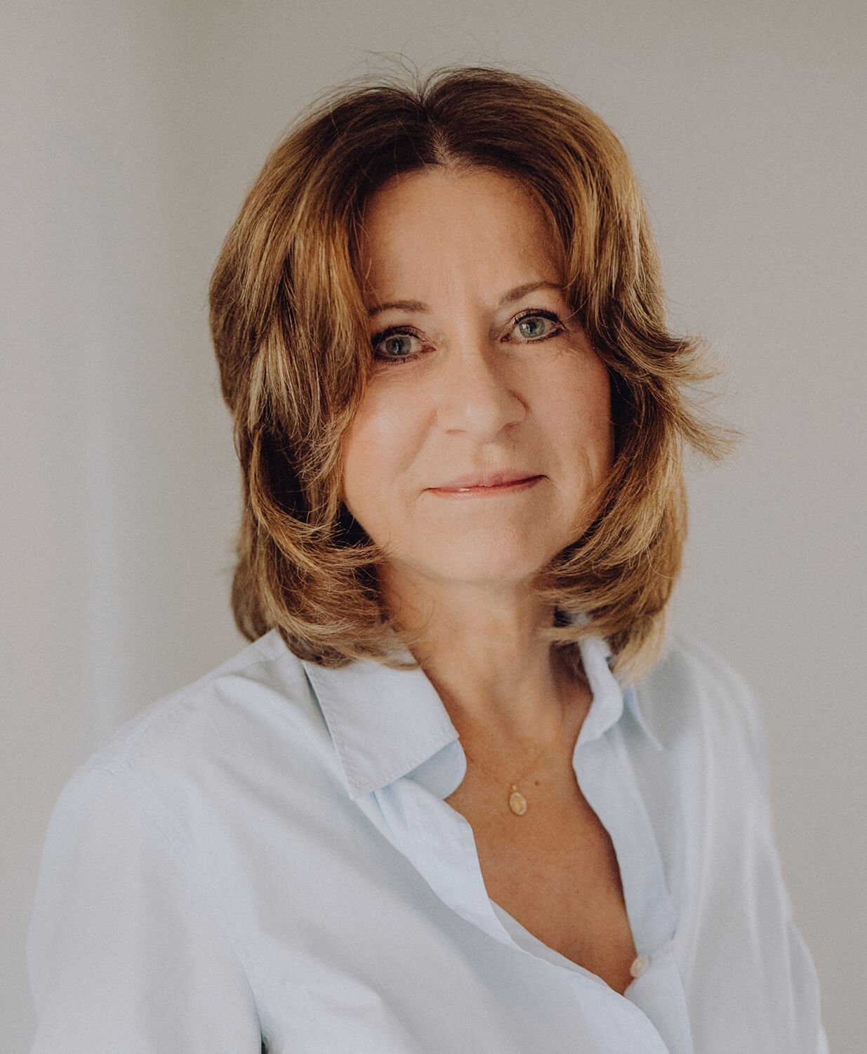 Ein Portrait Bild von Carola Brinkers sie schaut freundlich in die Kamera hat braune Schulterlange Haare und trägt eine helle Bluse.