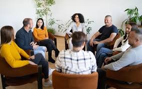 Group therapy session with eight diverse participants sitting in a circle and discussing.
