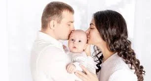 A family of three with a father, mother, and baby, facing each other closely.