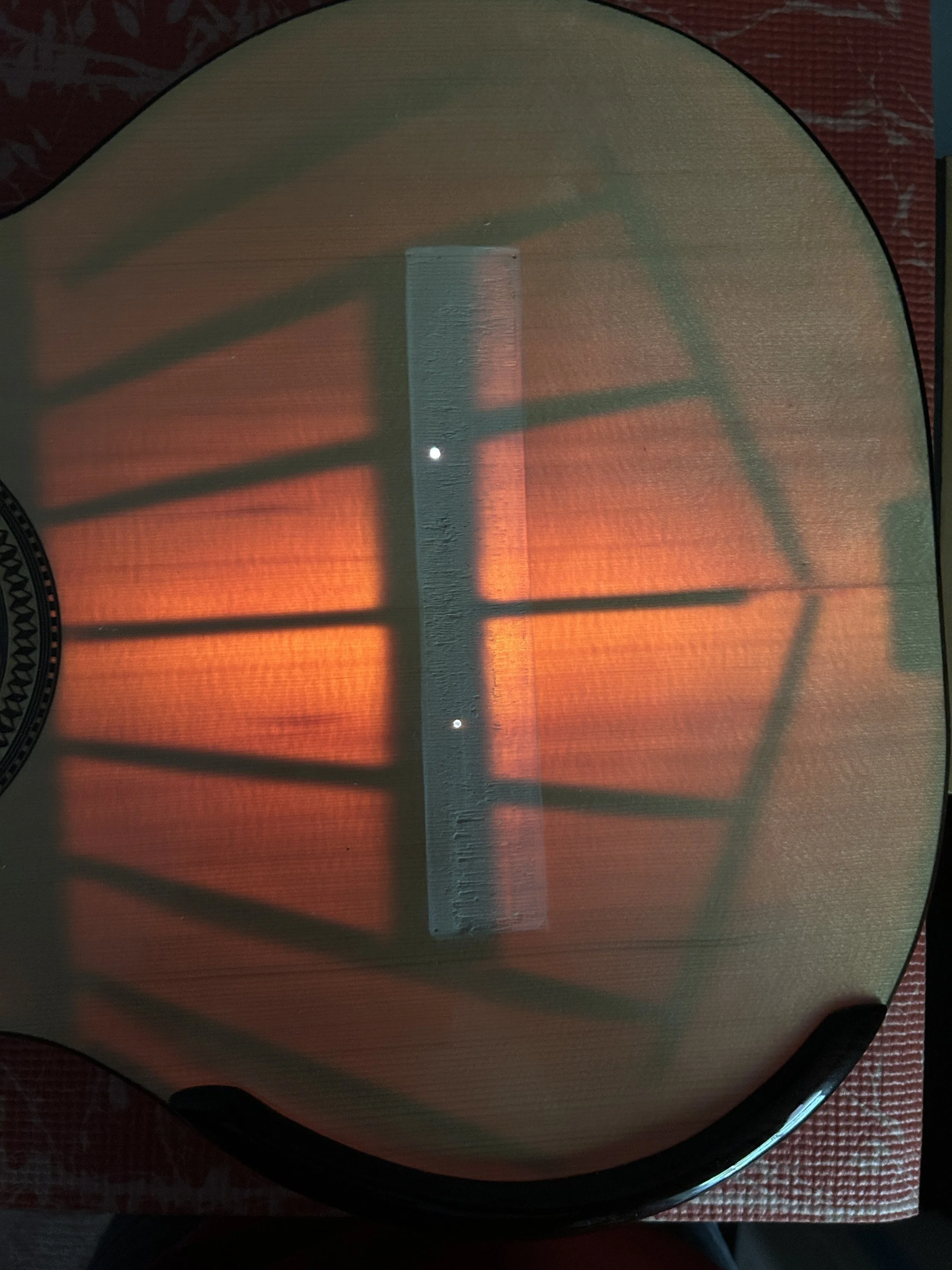 The shadow of a window with multiple rectangular panes is cast onto a surface illuminated by an orange light, creating a pattern of rectangles and lines.