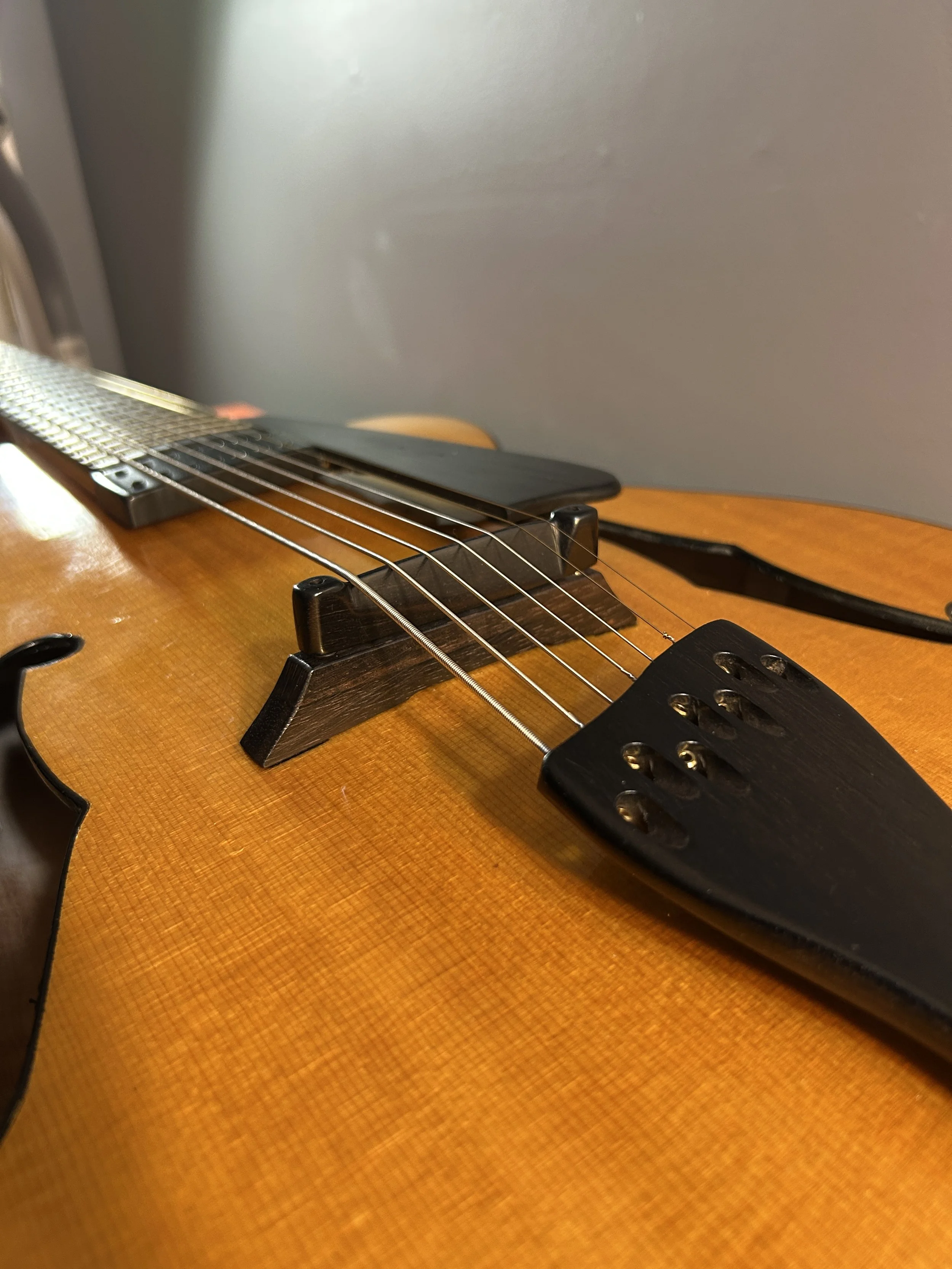 Close-up of an a Devoe acrhtop guitar with an ebony bridge and tailpiece.