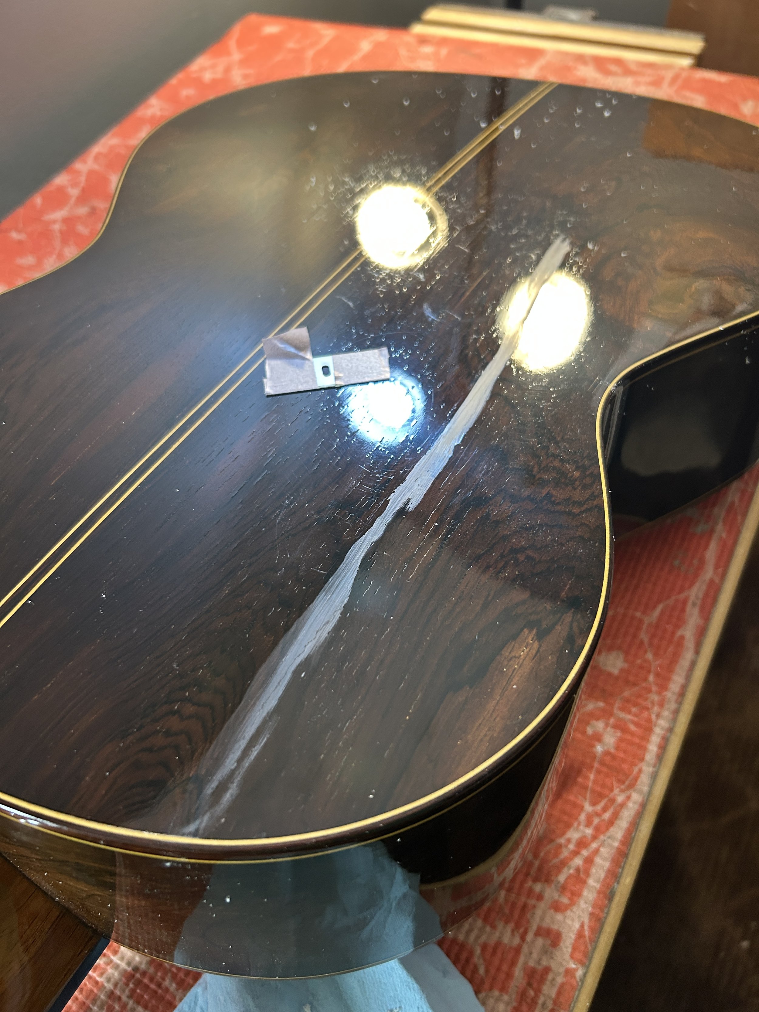 The back of an acoustic guitar with a crack being fixed and the finish being sanded.