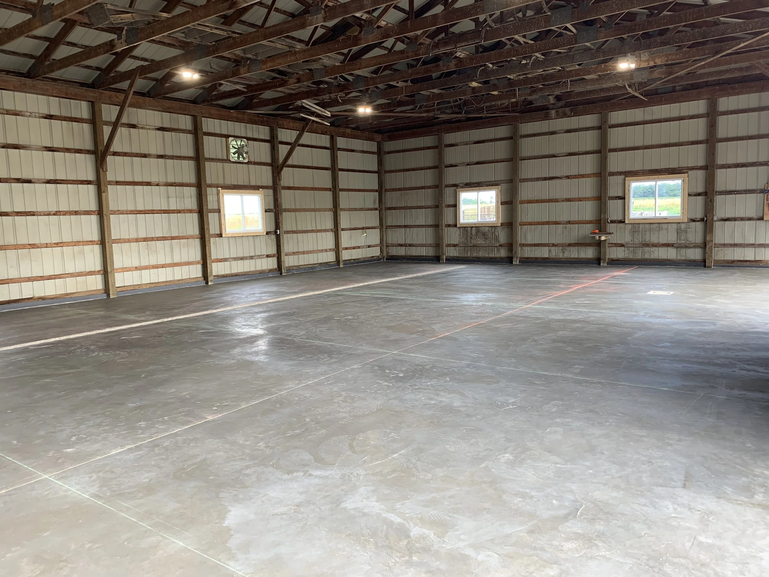 Empty garage with concrete floor, three small windows, and exposed wooden beams on the ceiling.