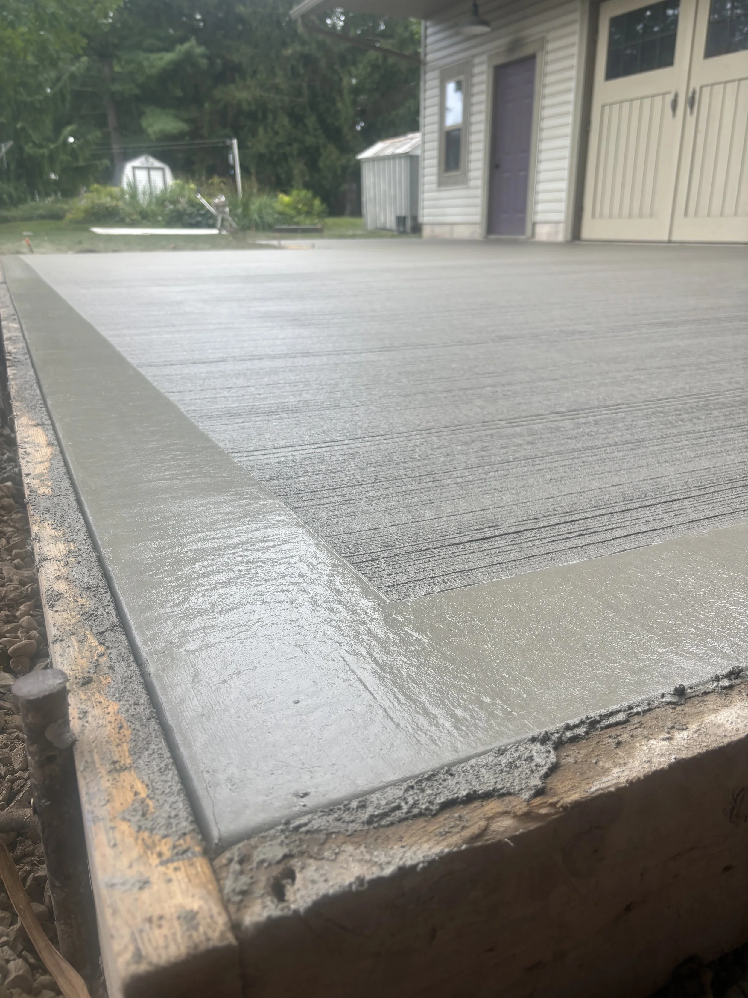 Close-up of a freshly poured concrete sidewalk with a textured surface next to a wooden form.