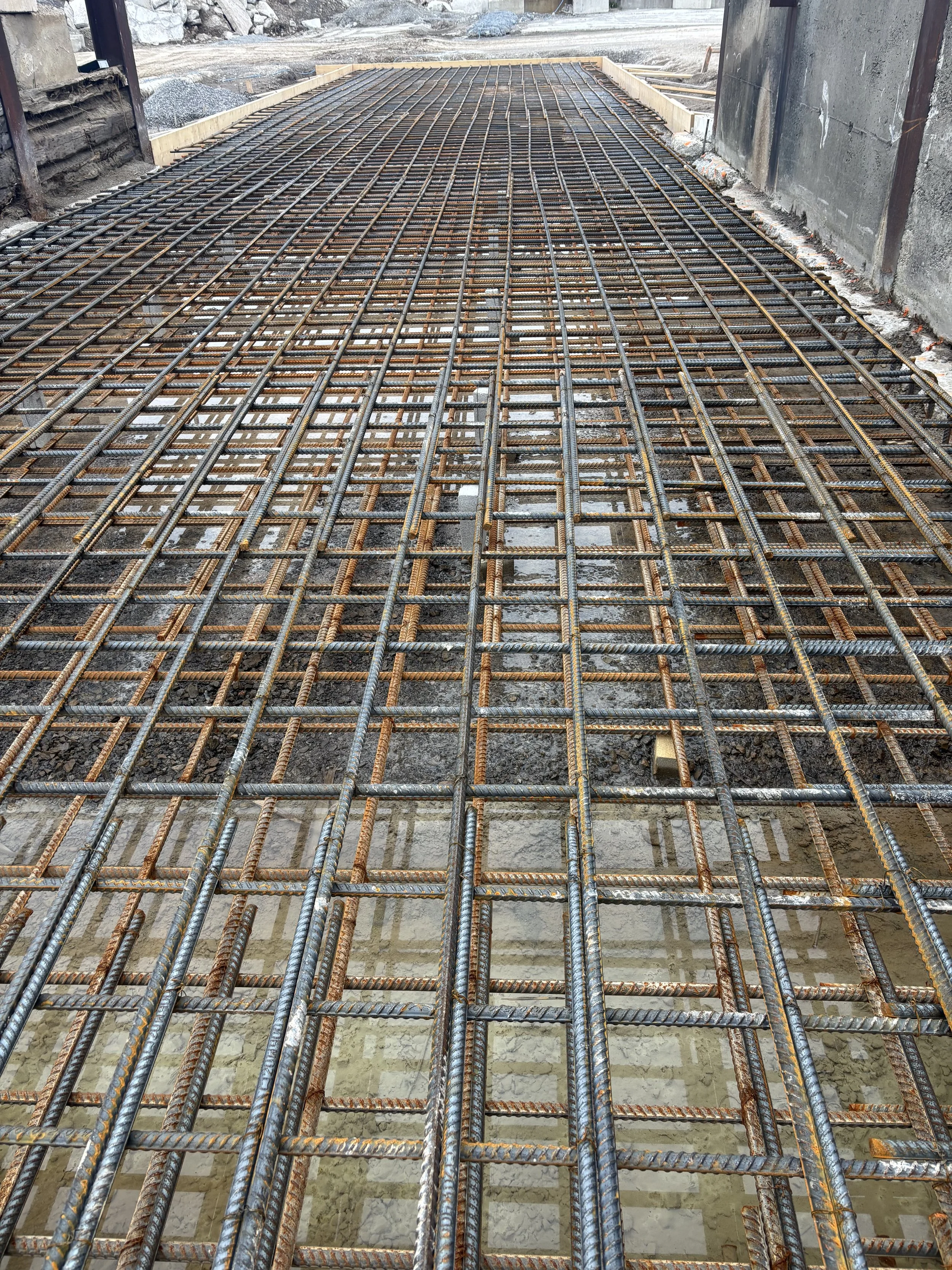 Steel rebar reinforcement arranged in a grid pattern for concrete pouring at a construction site.
