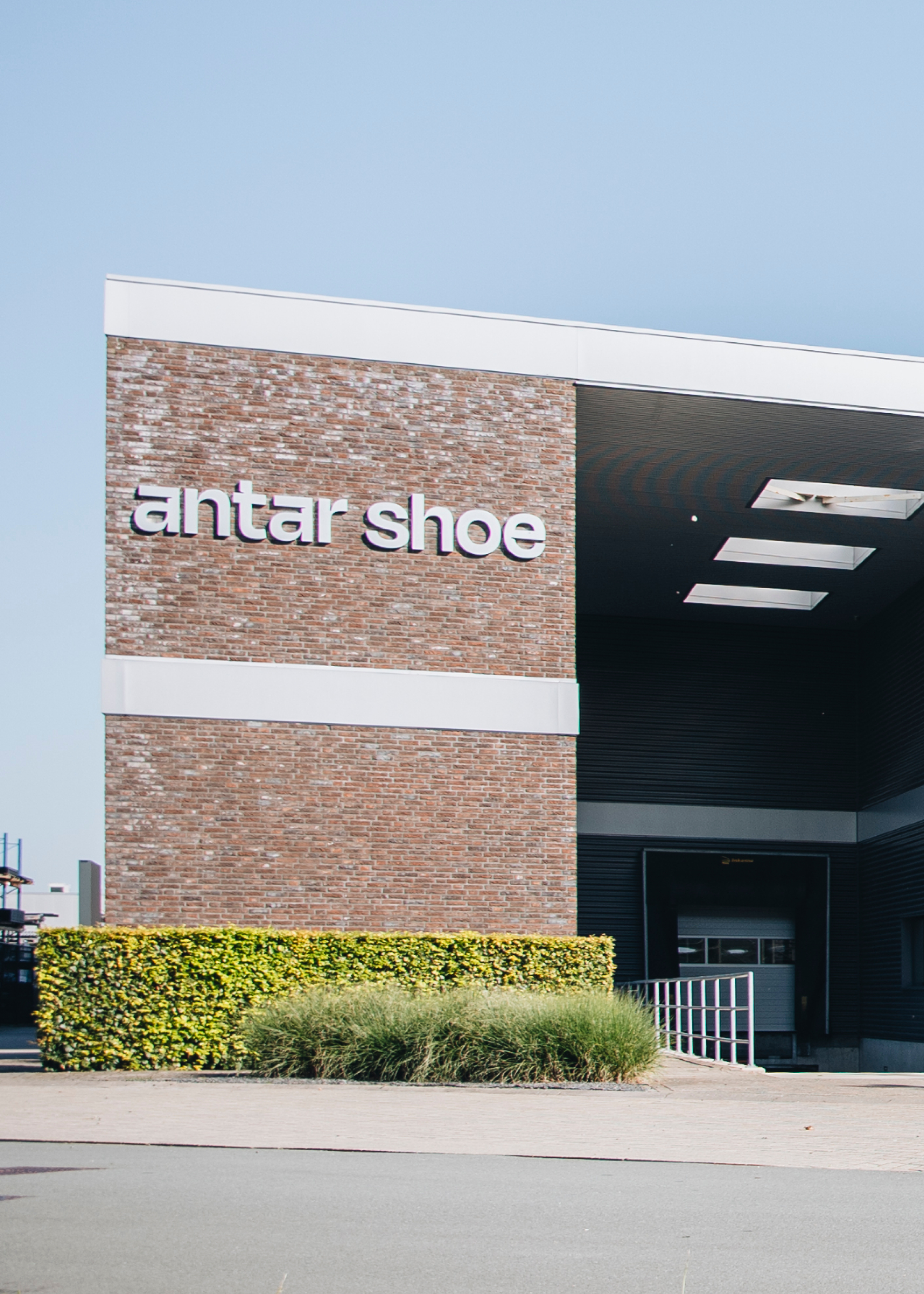 Exterior of an Anta Shoe store with brick wall, black panels, and white signage, surrounded by landscaping.