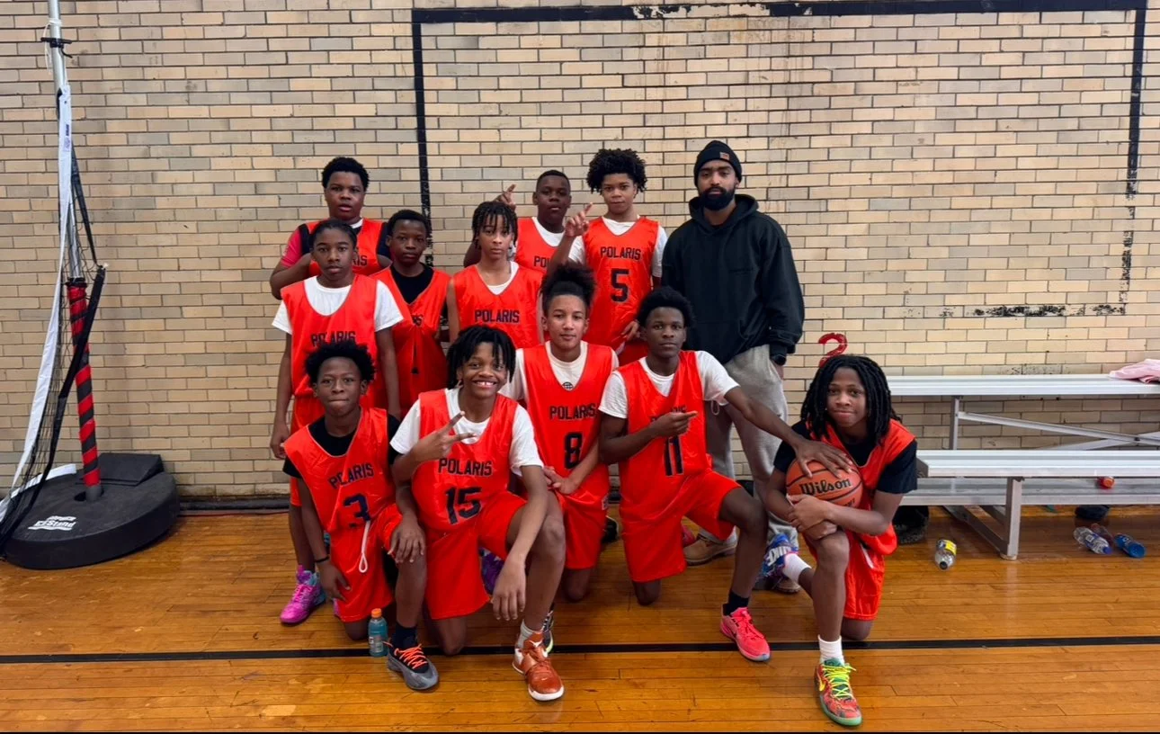 A youth basketball team in red uniforms posing with their coach in an indoor gym.