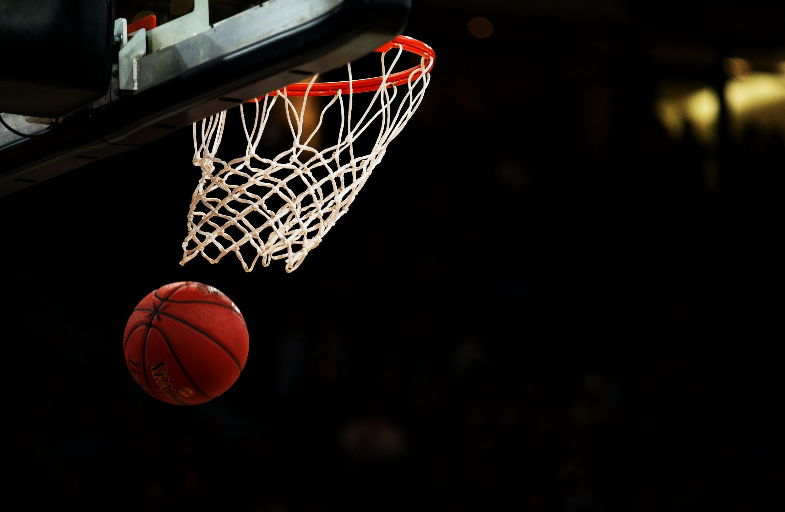 A basketball going through a basketball hoop against a dark background.