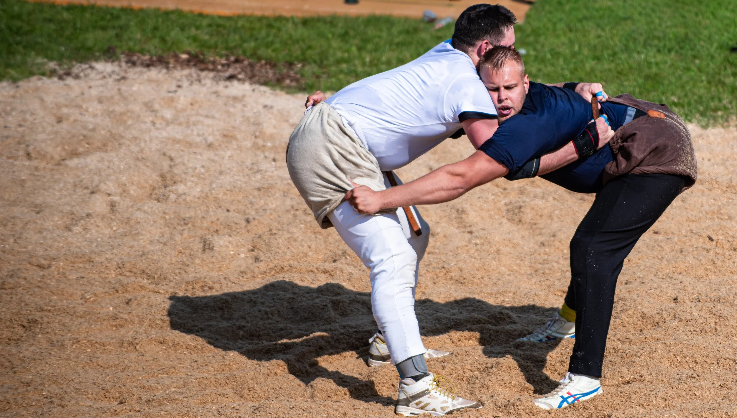 Zwei Männer beim Sambo-Kampfsportkampf auf dem Sand, einer versucht den anderen auf den Boden zu bringen.