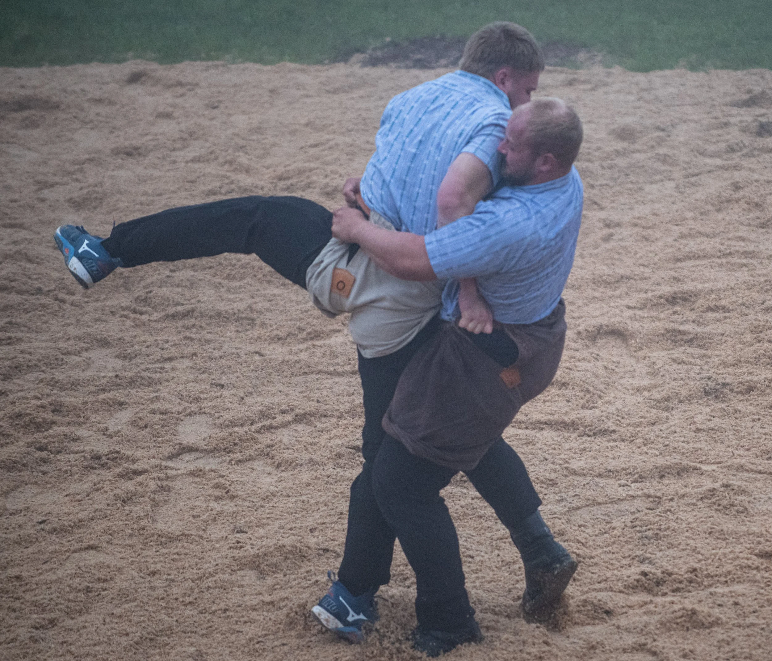 Zwei Männer heben sich bei einem Ringerwettkampf im Sand hoch, um zu kämpfen.