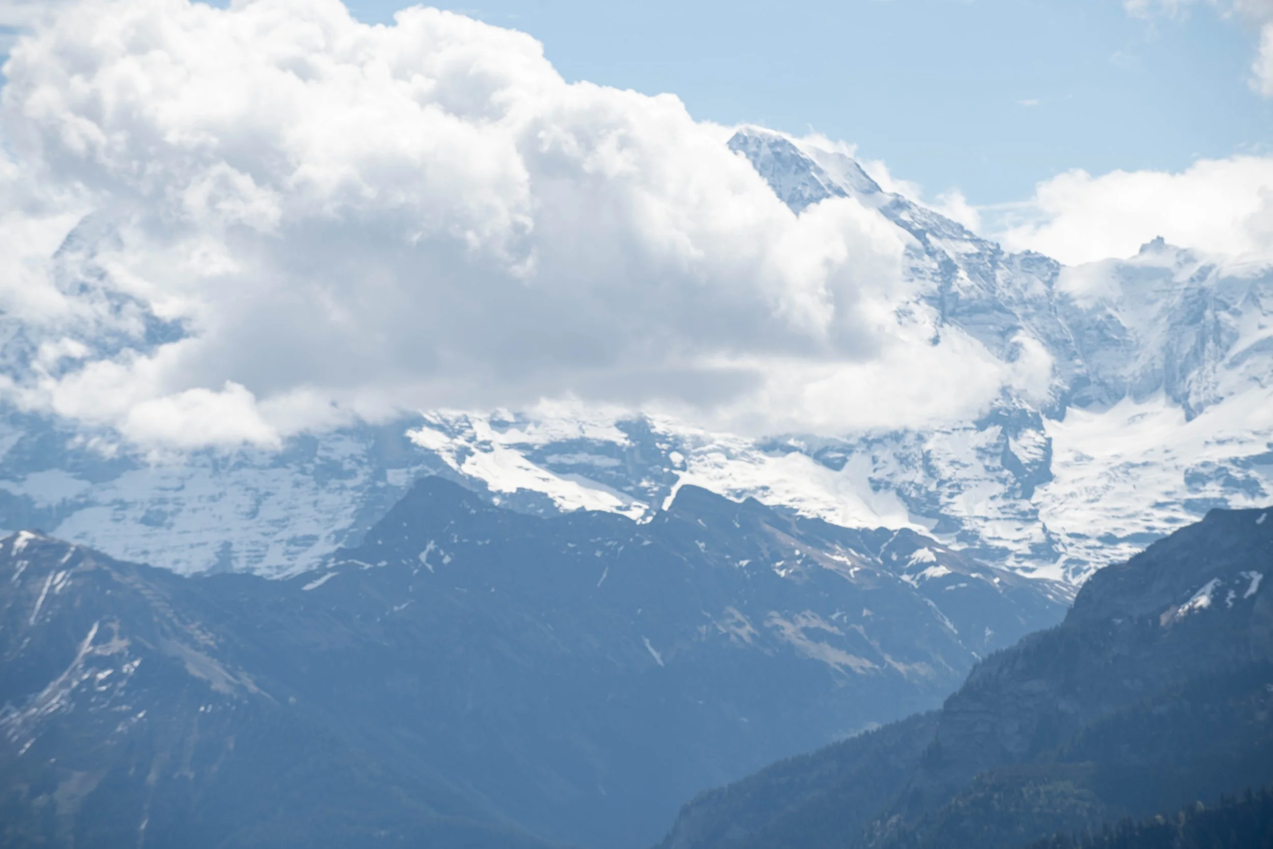 Schneebedeckte Berge hinter Wolken und blauen Himmel.