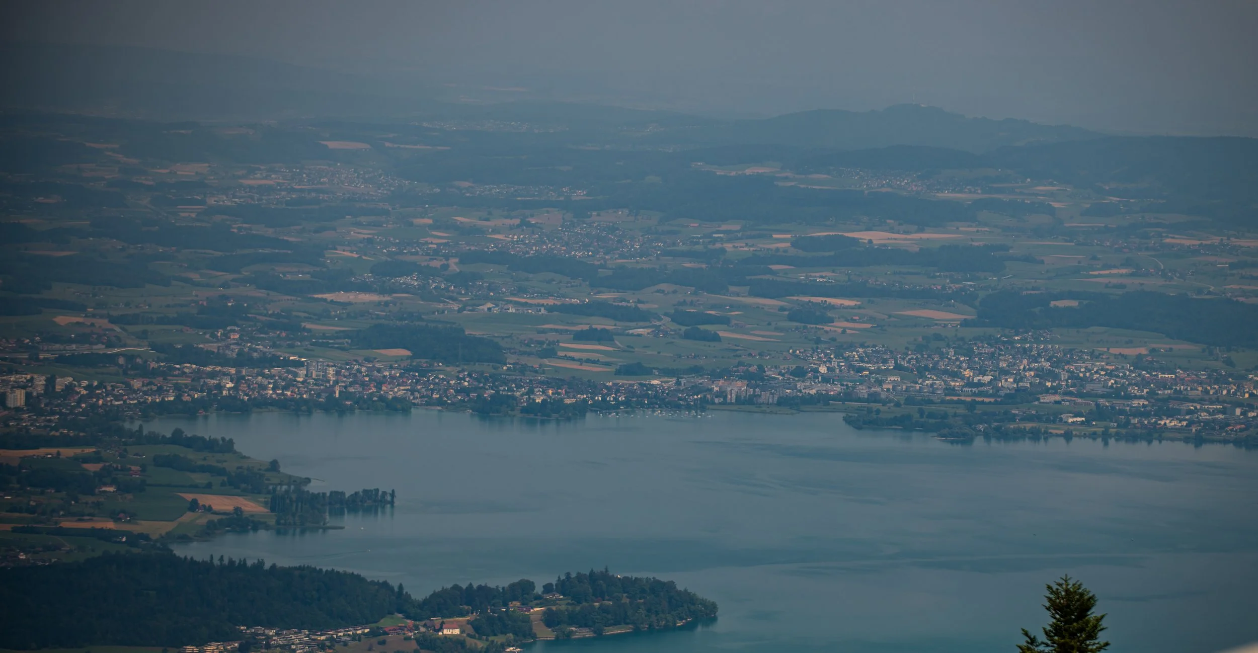 Landschaft mit Stadt, Wasser und Bergen im Hintergrund, bewölkter Himmel