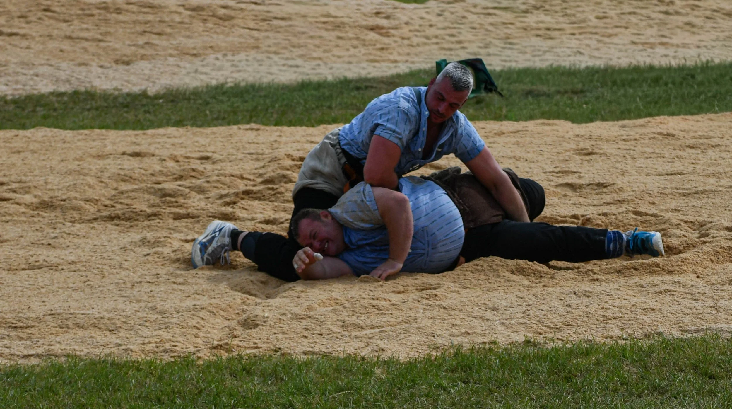 Zwei Männer während eines Kampfes auf einer Sandbahn. Einer liegt am Boden, während der andere ihn greift und zu Boden wirft.