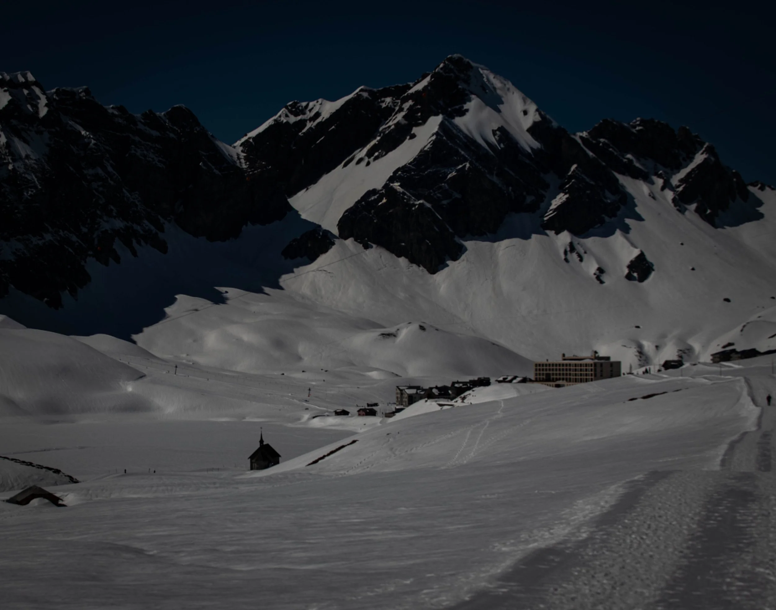 Schneebedeckte Berge bei Nacht mit kleinen Gebäuden im Vordergrund.