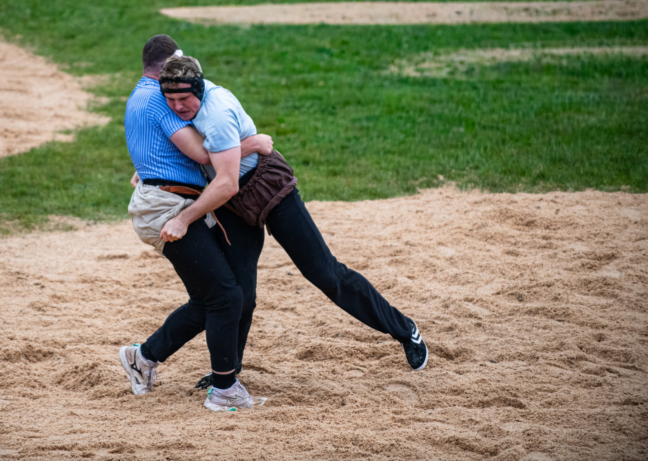 Zwei Männer kämpfen auf einem Baseballfeld, einer umklammert den anderen. Es sieht nach einer Szene während eines Spiels oder Trainings aus.