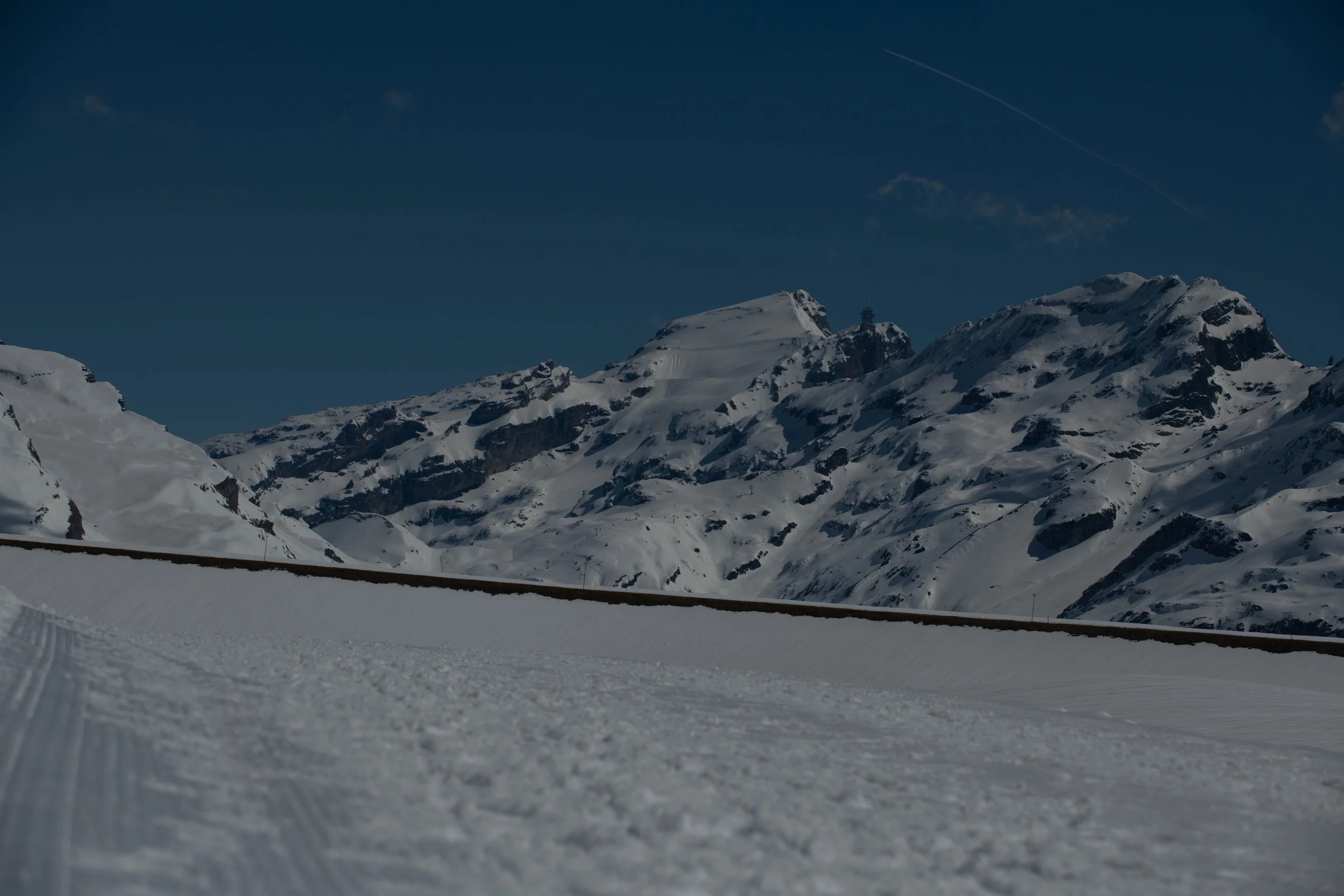 Blick auf verschneite Berggipfel unter klarem blauen Himmel, mit Skispuren im Vordergrund.