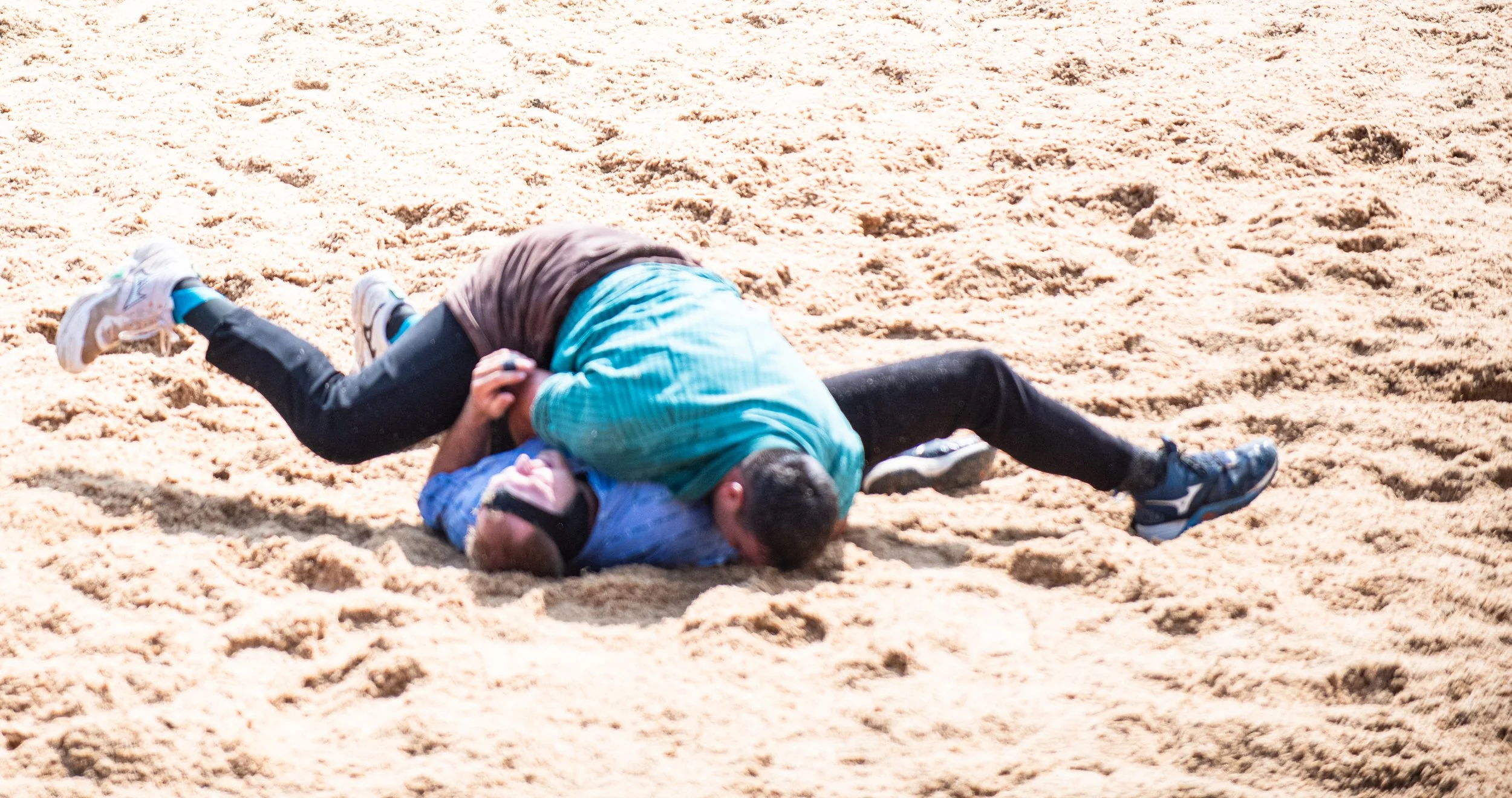 Zwei Männer beim Ringkampf auf Sand.