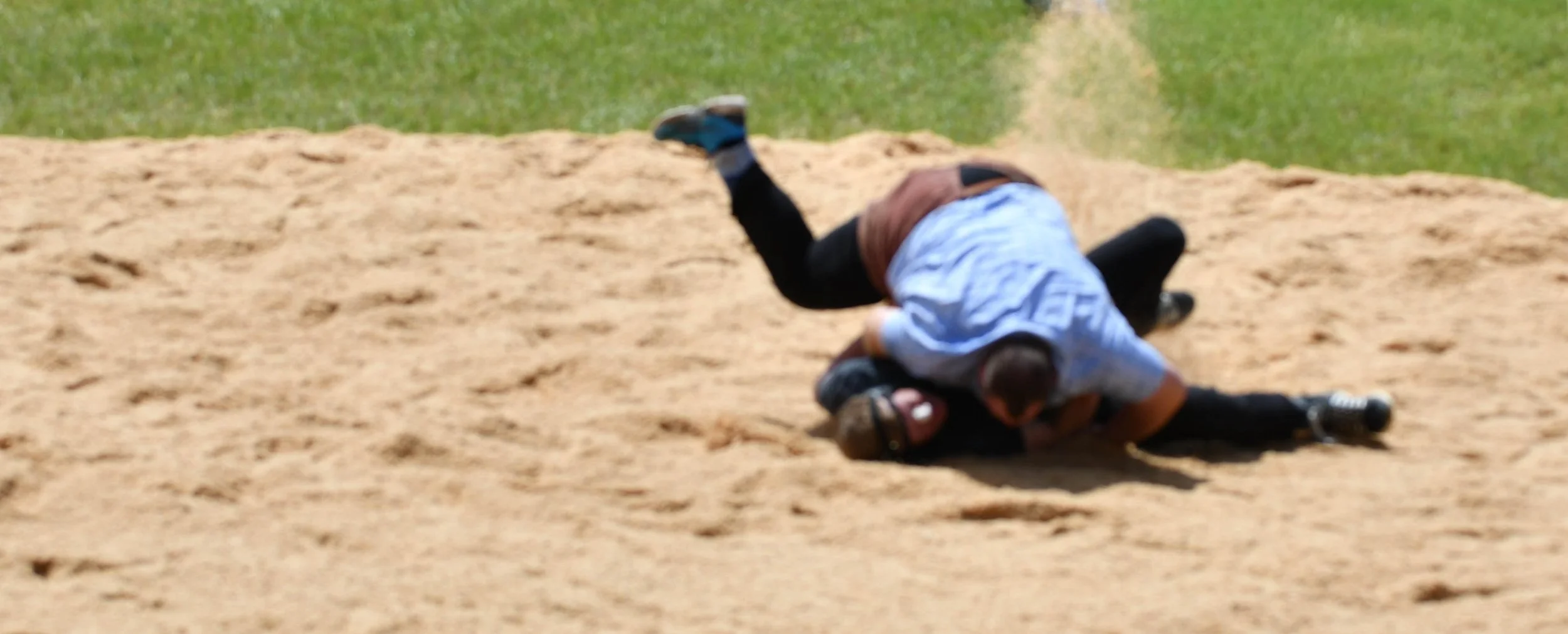 Zwei Kinder spielen auf einem Sandhügel; eines liegt auf dem Rücken, das andere ist darüber und hält es fest.