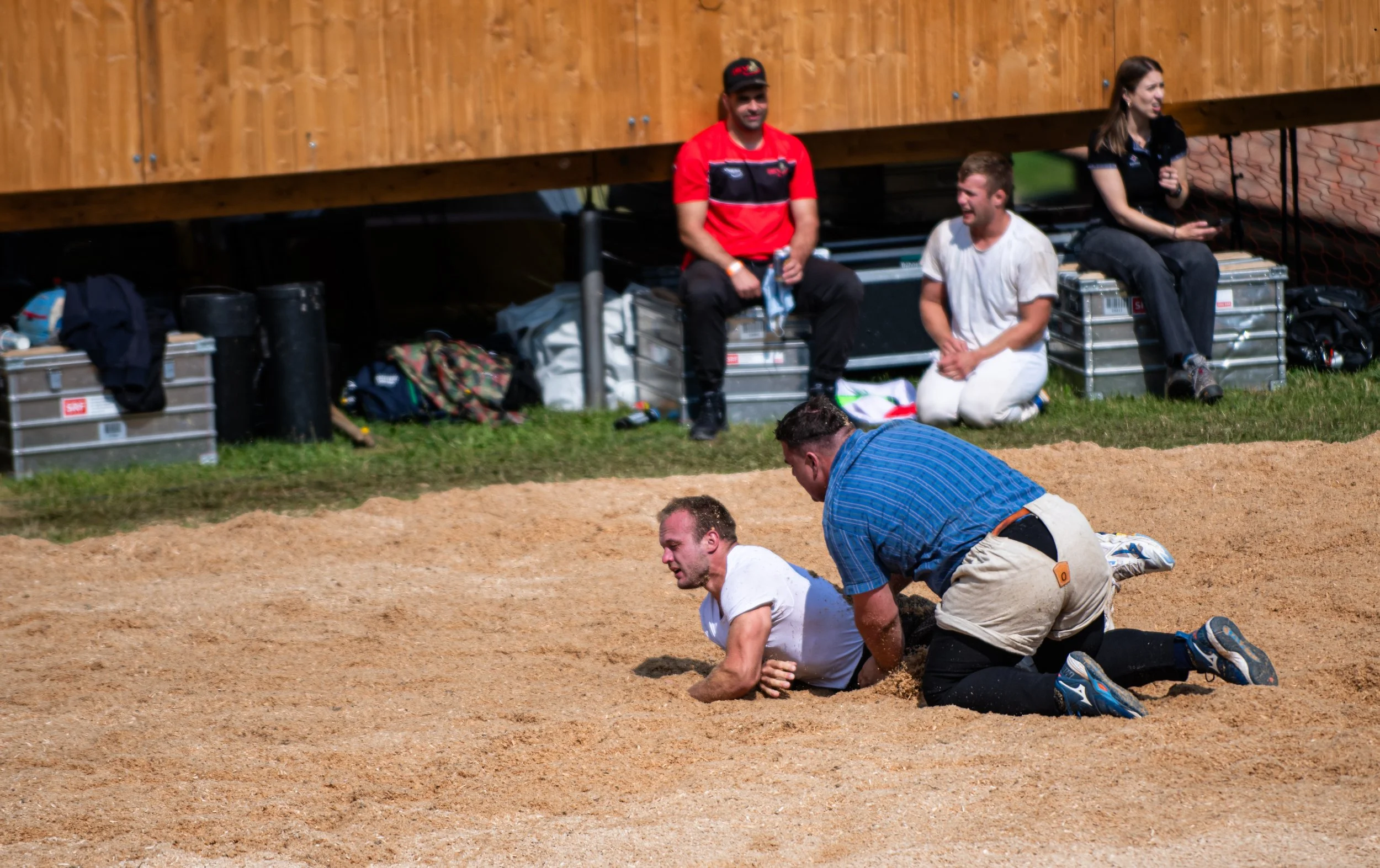 Menschen, die beim Wettkampf im Sand nahe einer Holzwand und On-Board-Equipment sitzen und sich auf das Rennen vorbereiten.