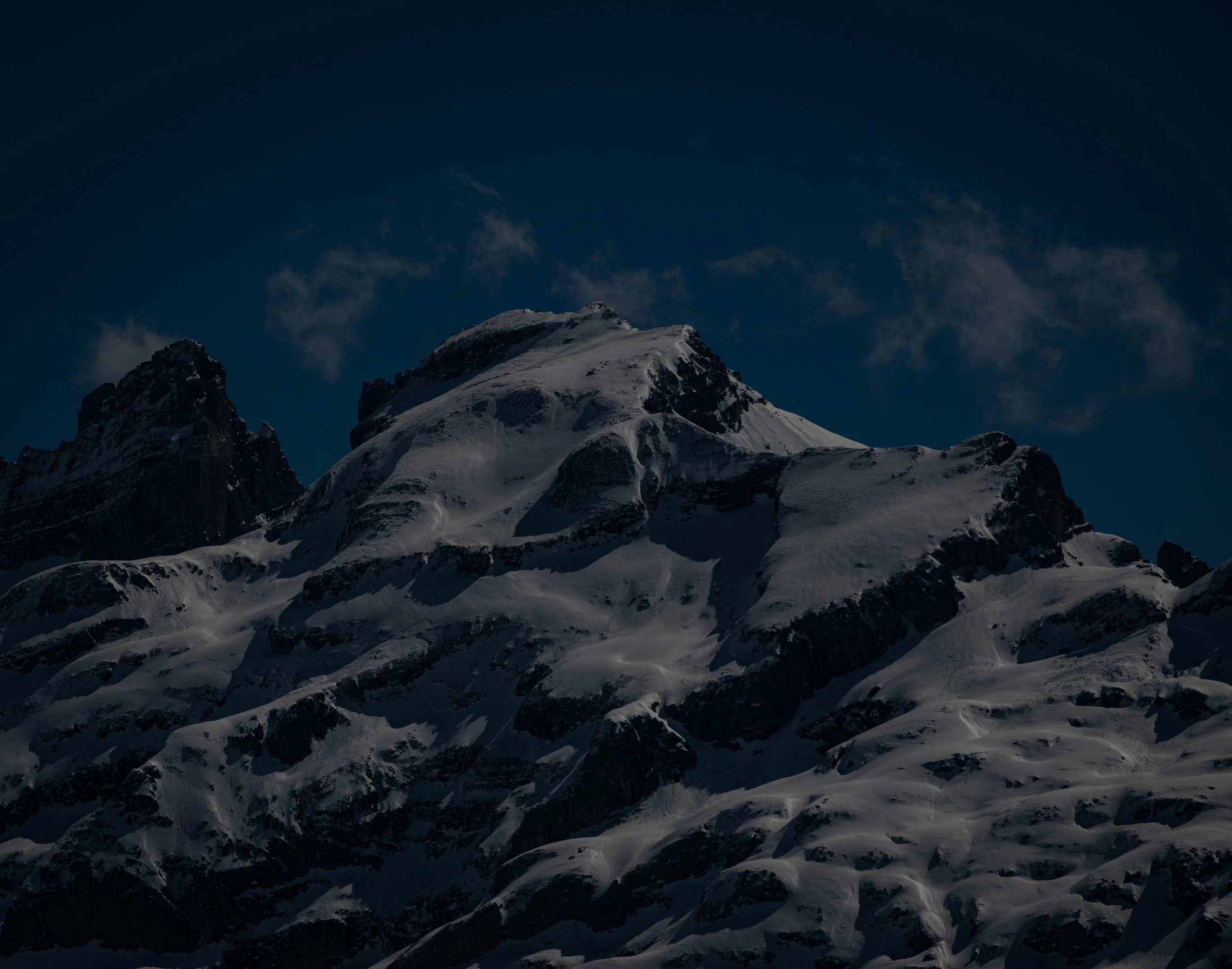 Eine verschneite Berglandschaft bei Nacht mit dunklem Himmel und wenigen Wolken.