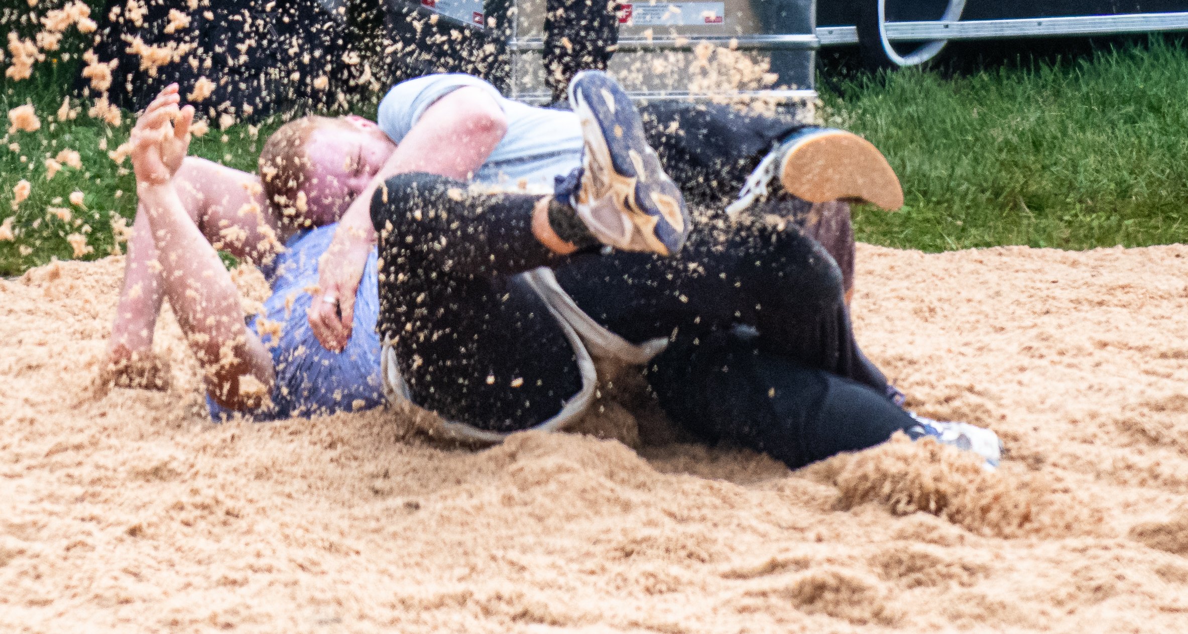 Zwei Personen, die beim Wrestling auf Sandboden gefallen sind, kämpfen auf dem Boden, umkämpfen sich und werfen Sand hoch