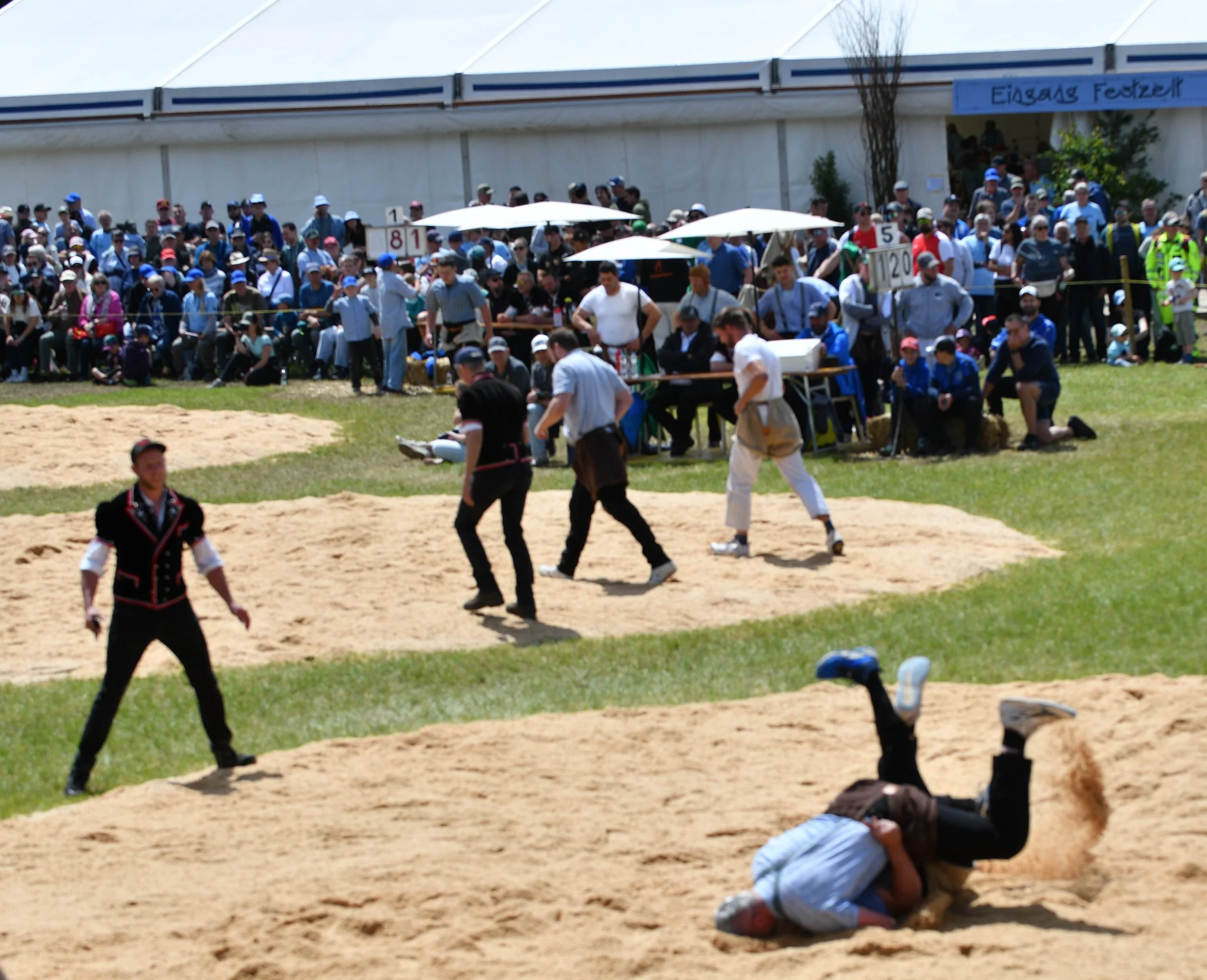 Menschen bei einem historischen Turnier, einige im traditionellen Kampfsport-Kostüm, im Freien vor einem großen weißen Zelt.