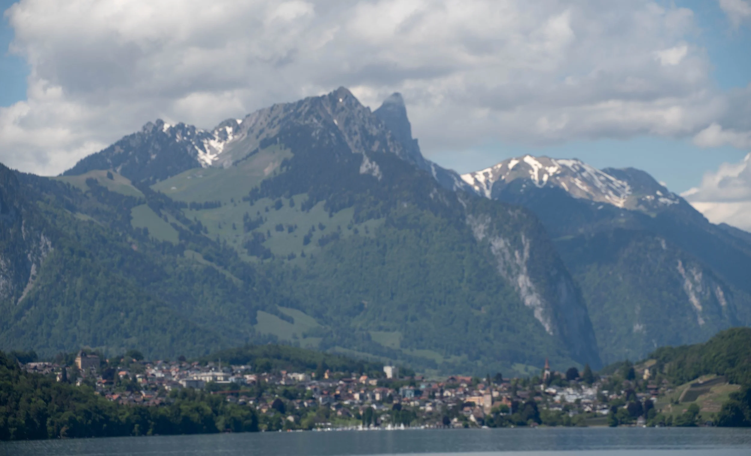 Berg mit schneebedeckten Gipfeln, im Vordergrund ein See und ein Dorf an der Küste.