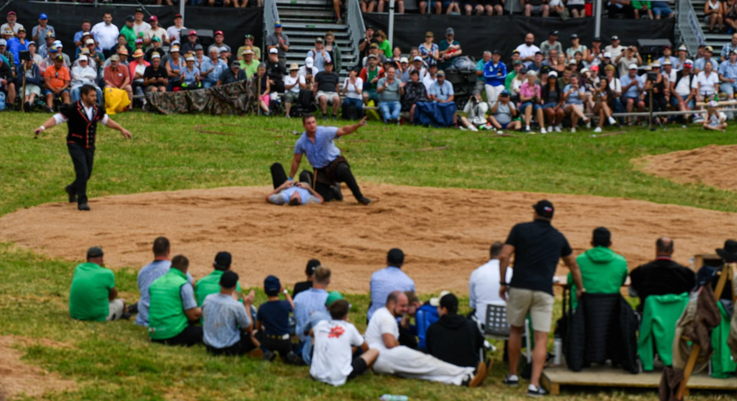 Bodenständiger Zirkus- oder Straßentheaterauftritt vor einer großen Menschenmenge, die auf Sitzgelegenheiten im Freien sitzt.