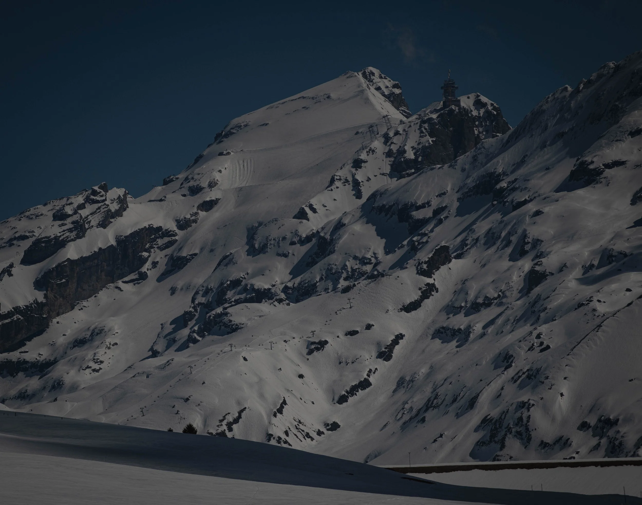 Schnee bedeckte Berge mit Skiliften und einer Bergstation unter einem klaren Himmel, vermutlich in den Alpen.
