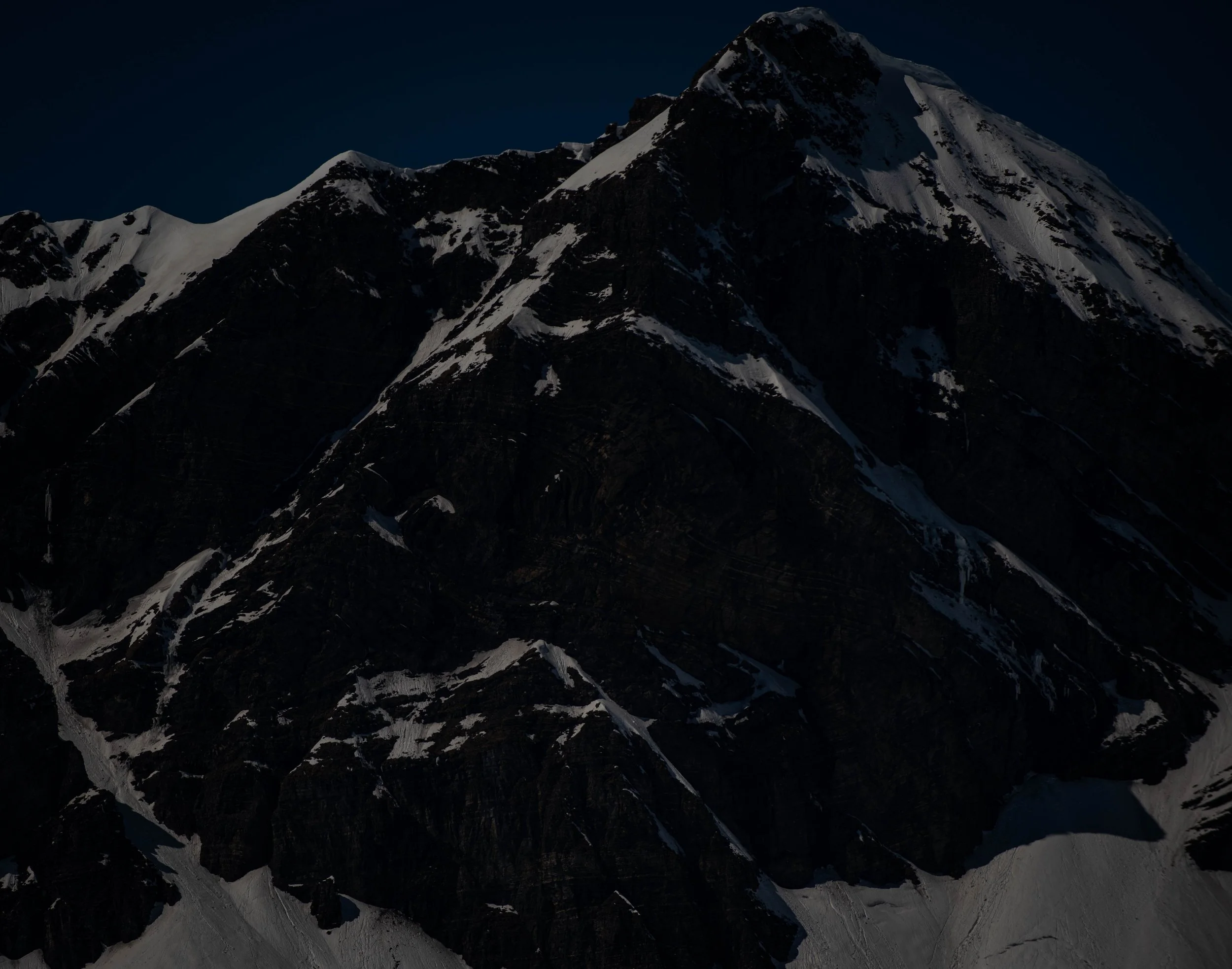 Schneebedeckte Berggipfel unter einem dunklen Himmel bei Nacht.