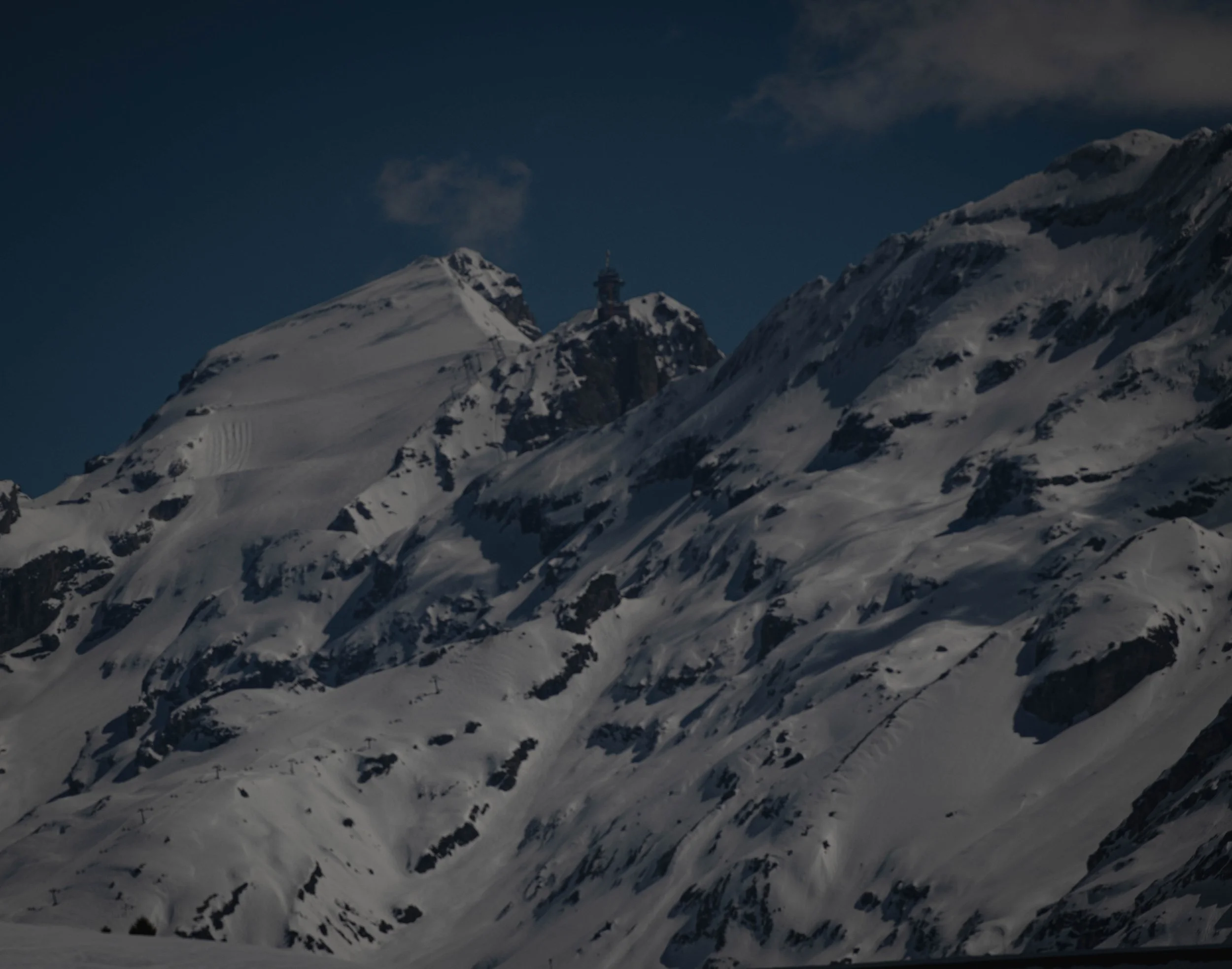 Schneebedeckte Berge unter einem dunklen Himmel mit wenigen Wolken.
