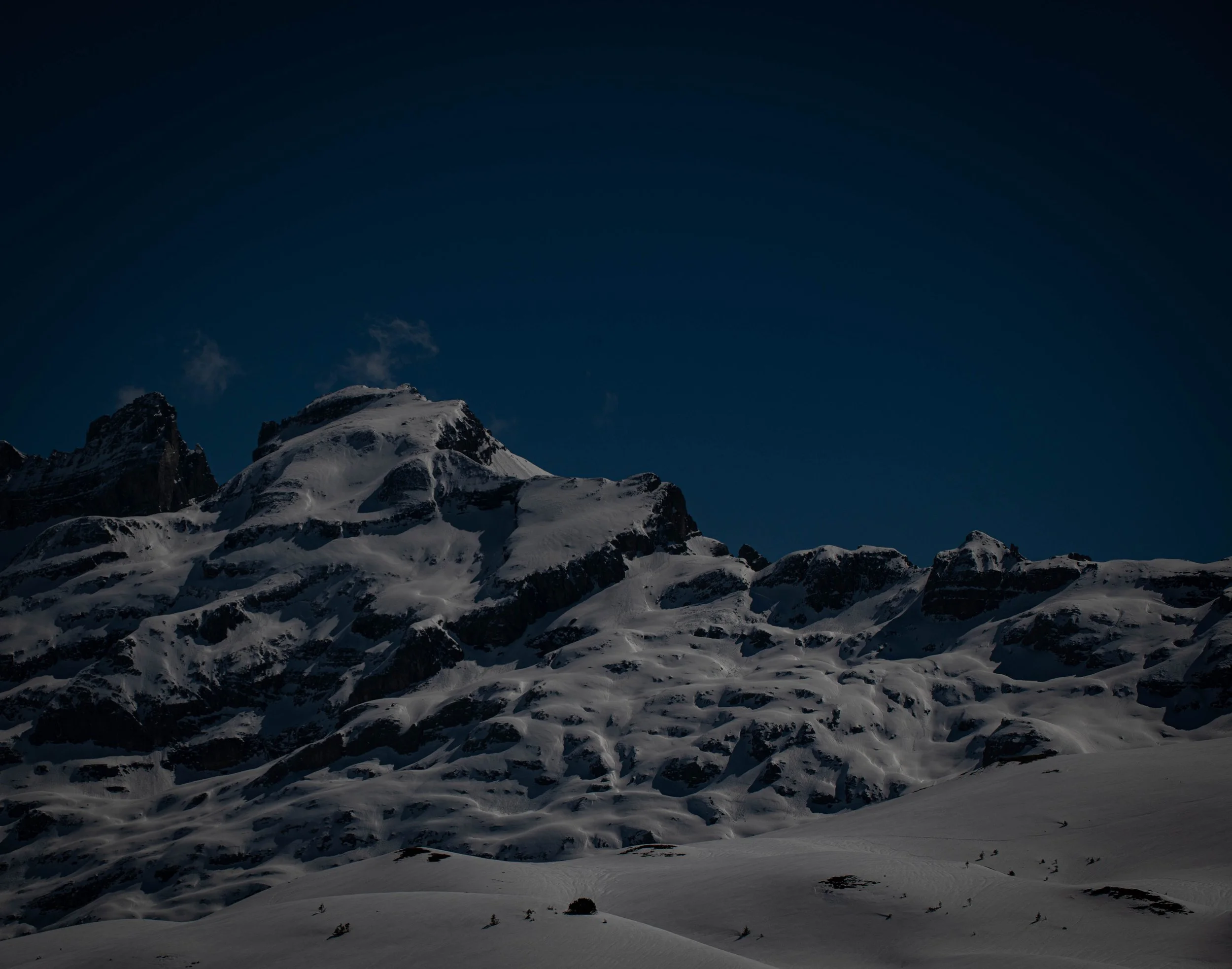 Schneebedeckte Berge bei Nacht mit dunklem Himmel.